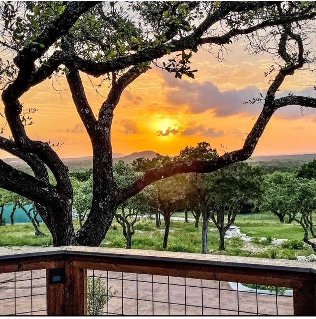 Sunset over a landscape with trees, a wooden railing in the foreground, and a colorful sky with clouds.