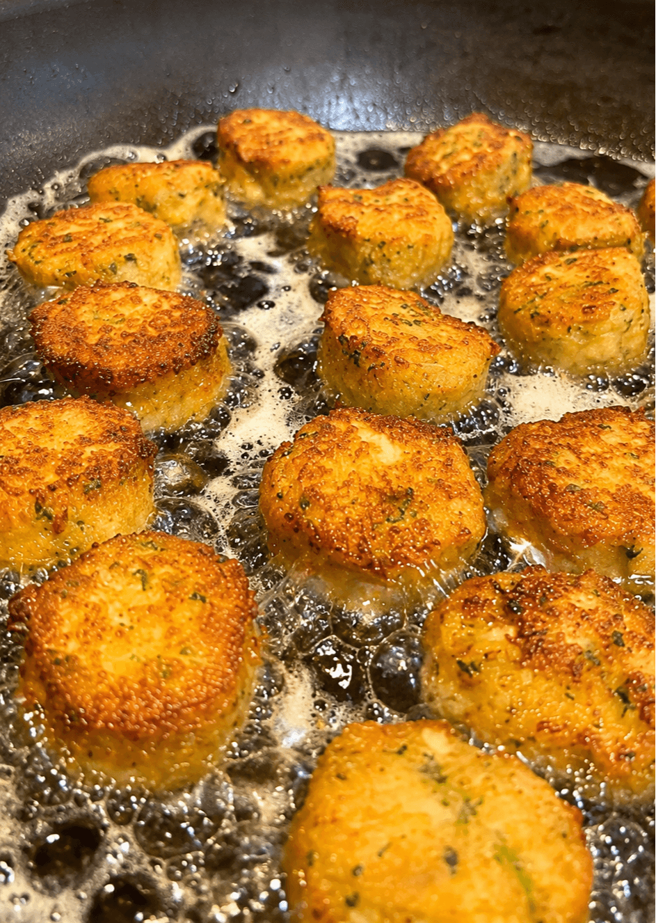 Fried food balls cooking in hot oil in a pan, golden brown and crispy, bubbling oil around them.