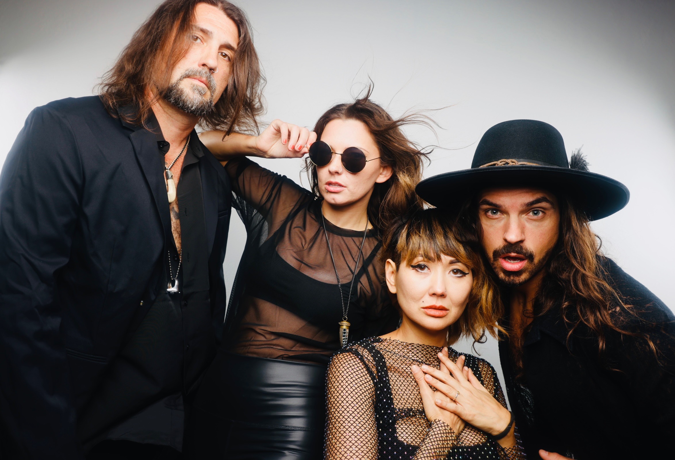 Group of four people posing, two women and two men, with varied hairstyles and clothing, against a plain background.