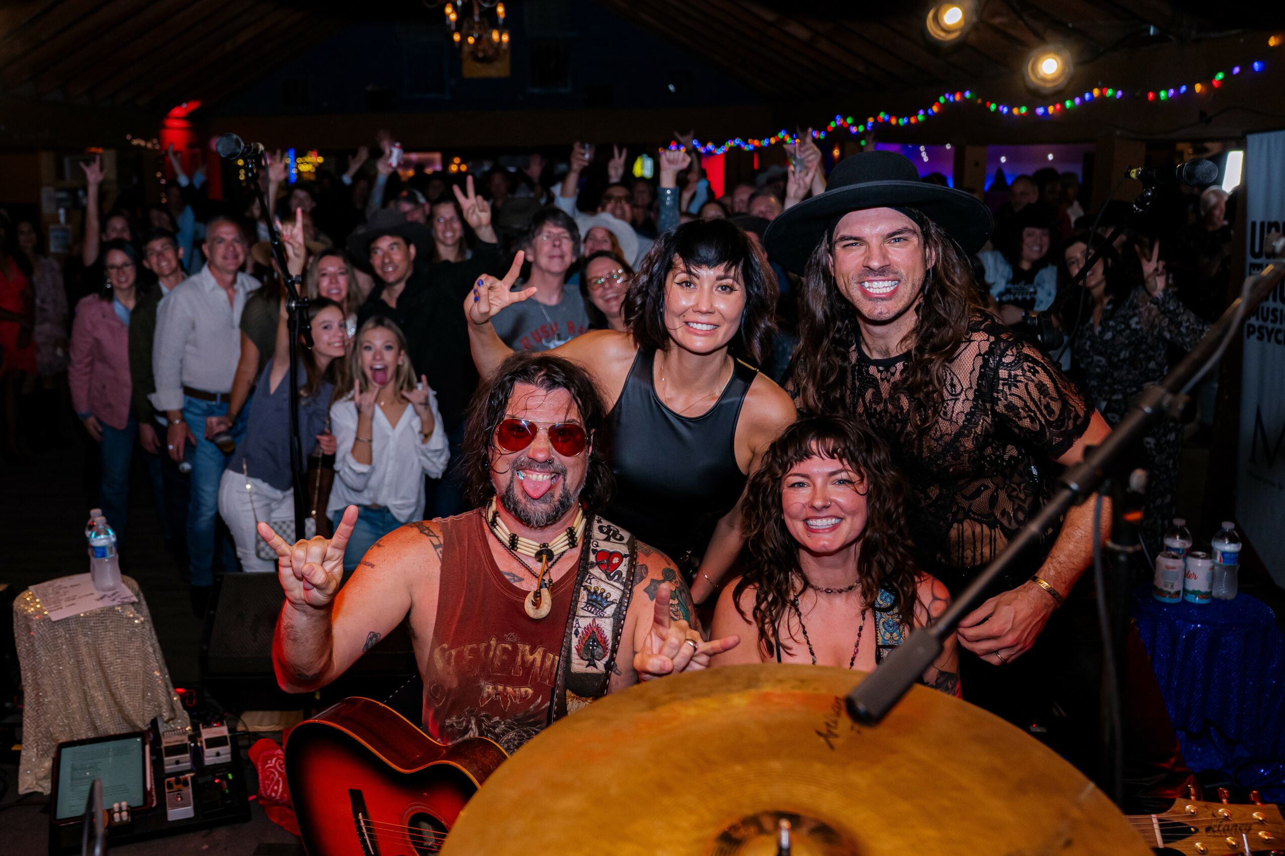 Four people in costumes pose for a photo at a crowded event with colorful lights and people in the background.