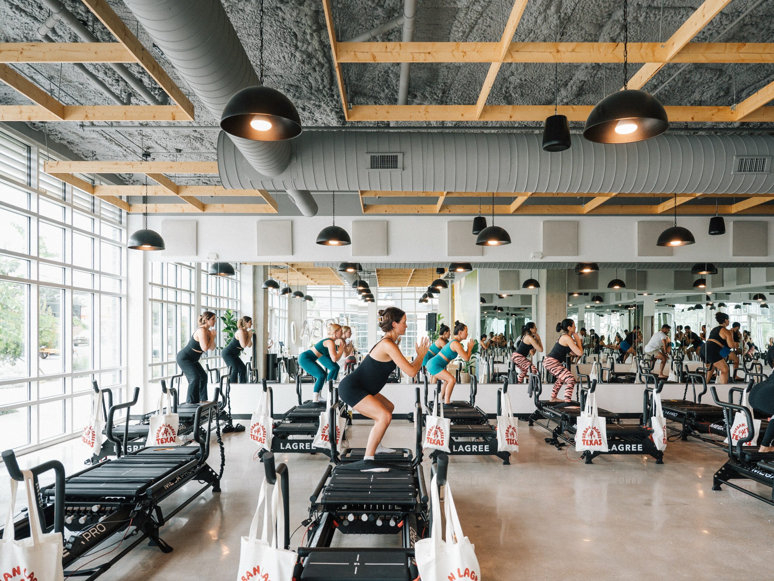 People exercising on treadmills in a spacious gym with large windows and high ceilings.