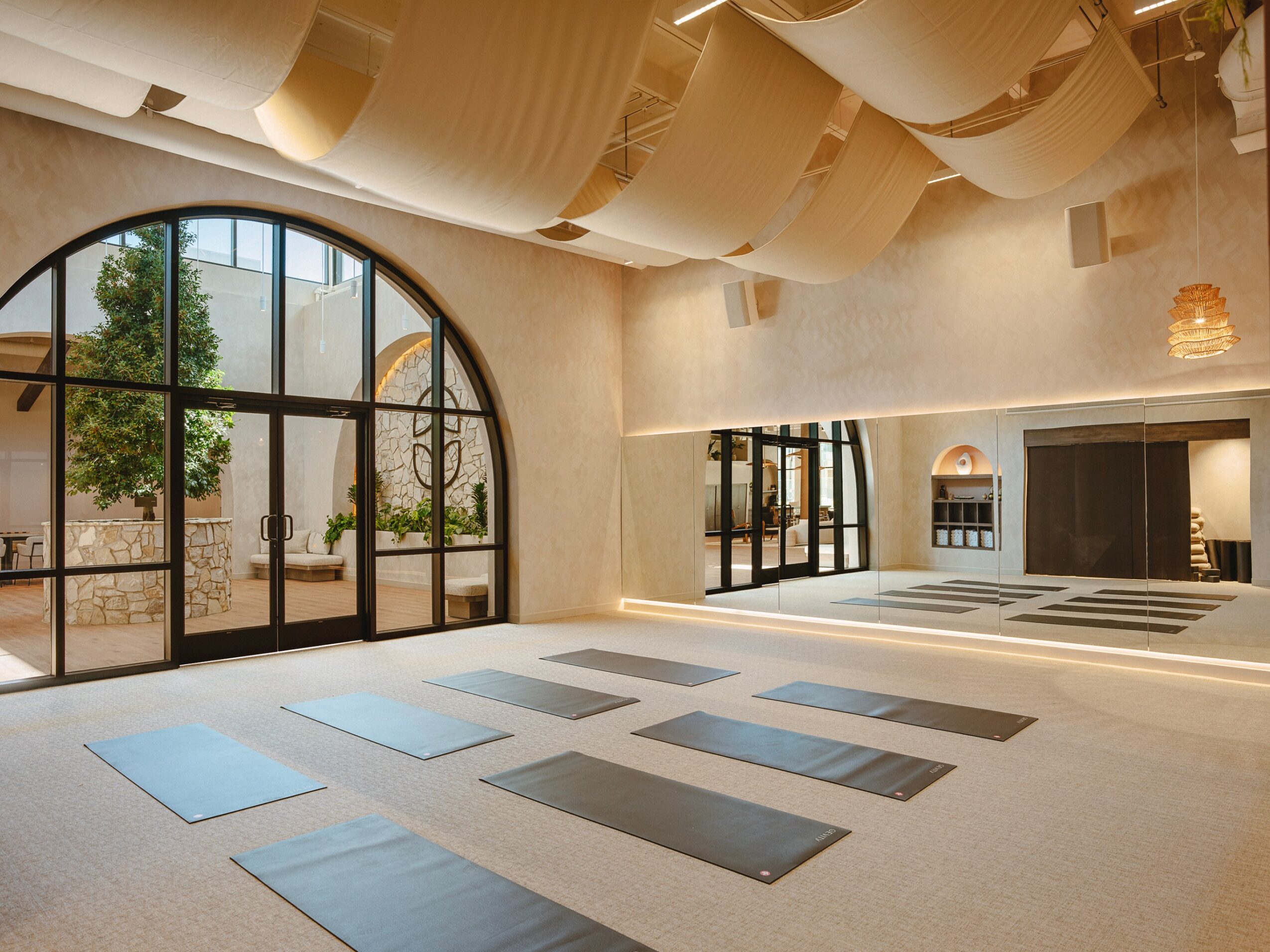 Indoor space with large arched windows, yoga mats on the floor, and ceiling fabric decorations, bright and airy.