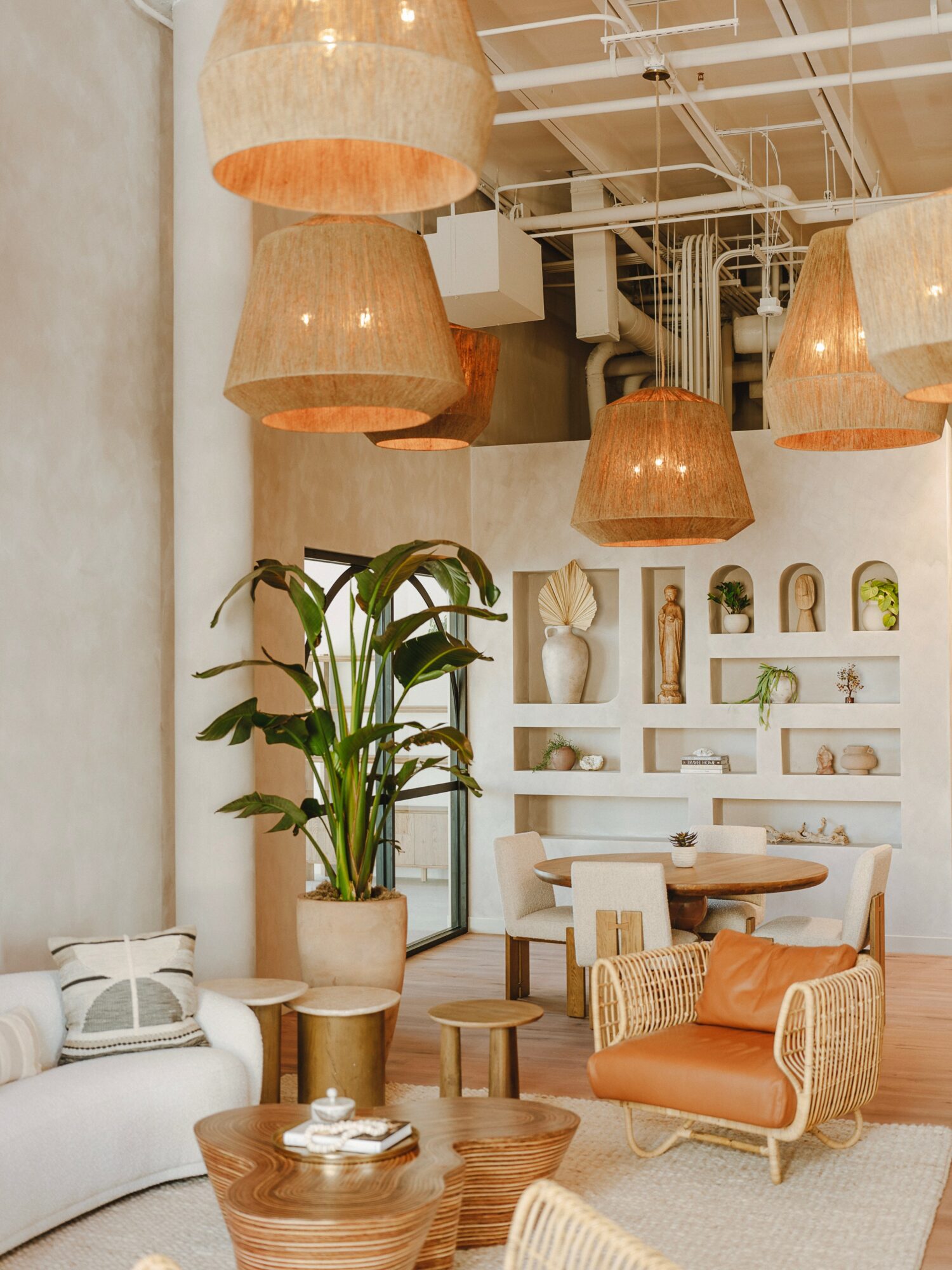 Interior space with hanging lamps, a large potted plant, white shelving, and seating including a white sofa and an orange armchair.