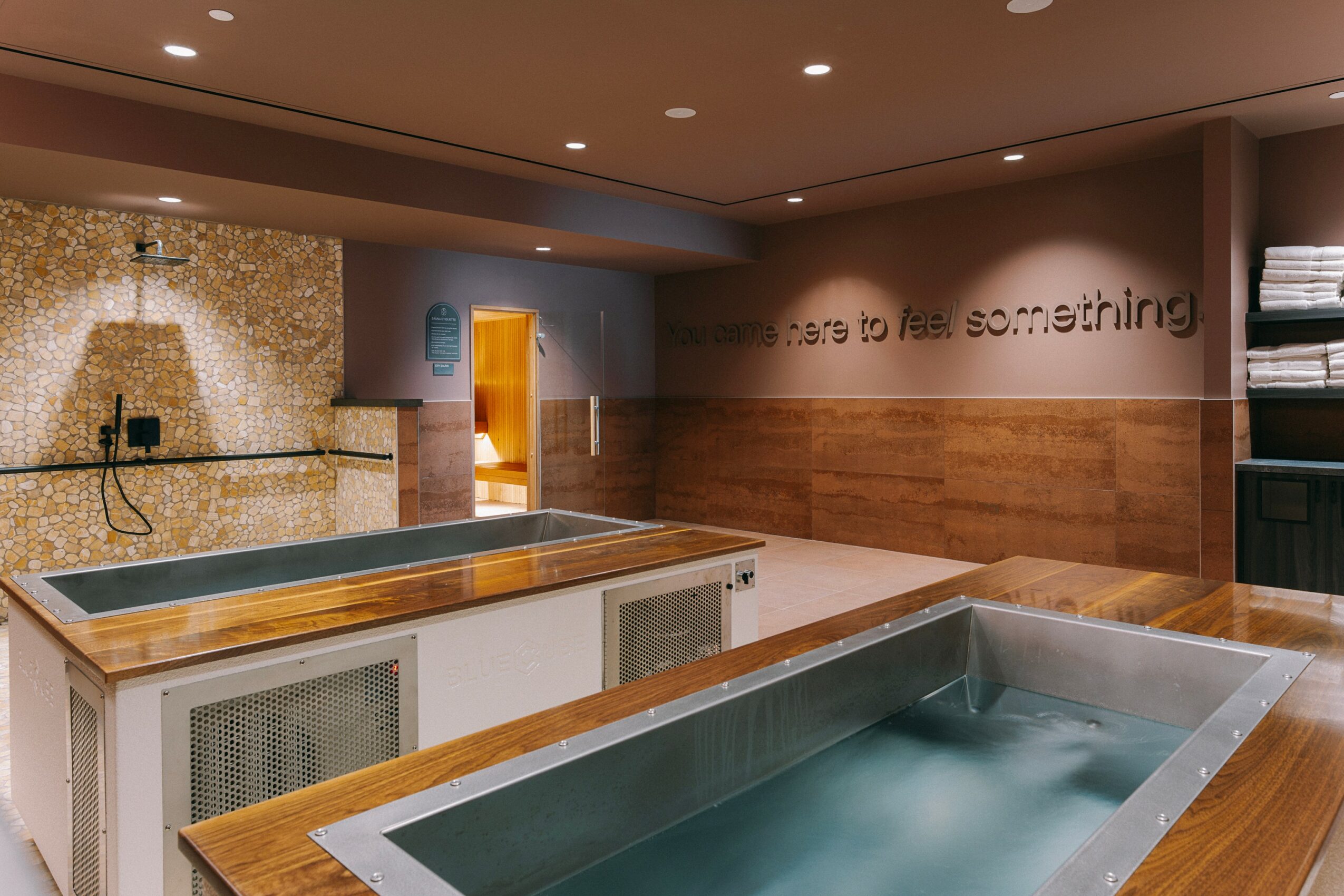 Indoor space with a large wooden table, a wall with text, and a shower area in the background.