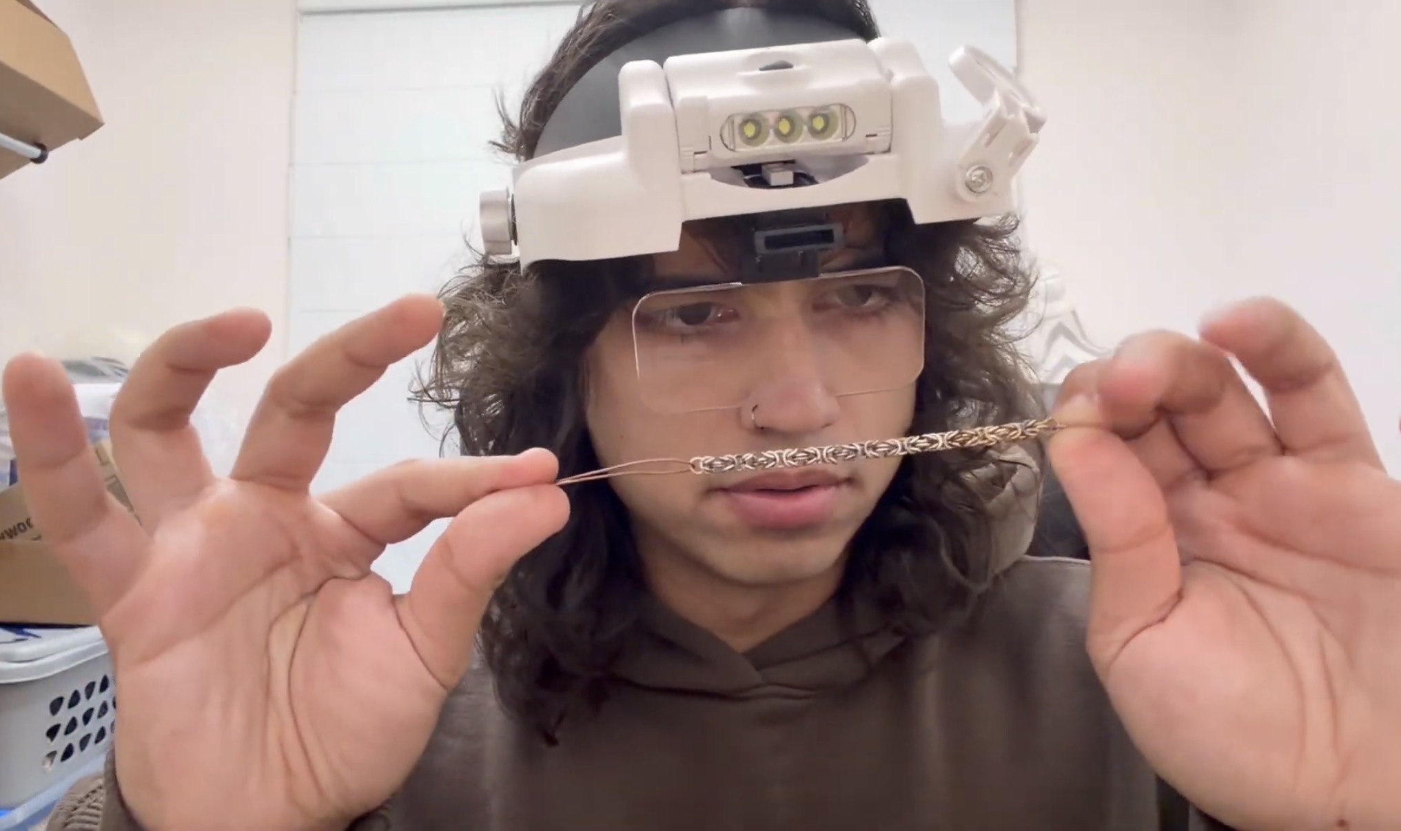 Person wearing a headlamp and glasses, holding a thin object horizontally, with a focused expression.