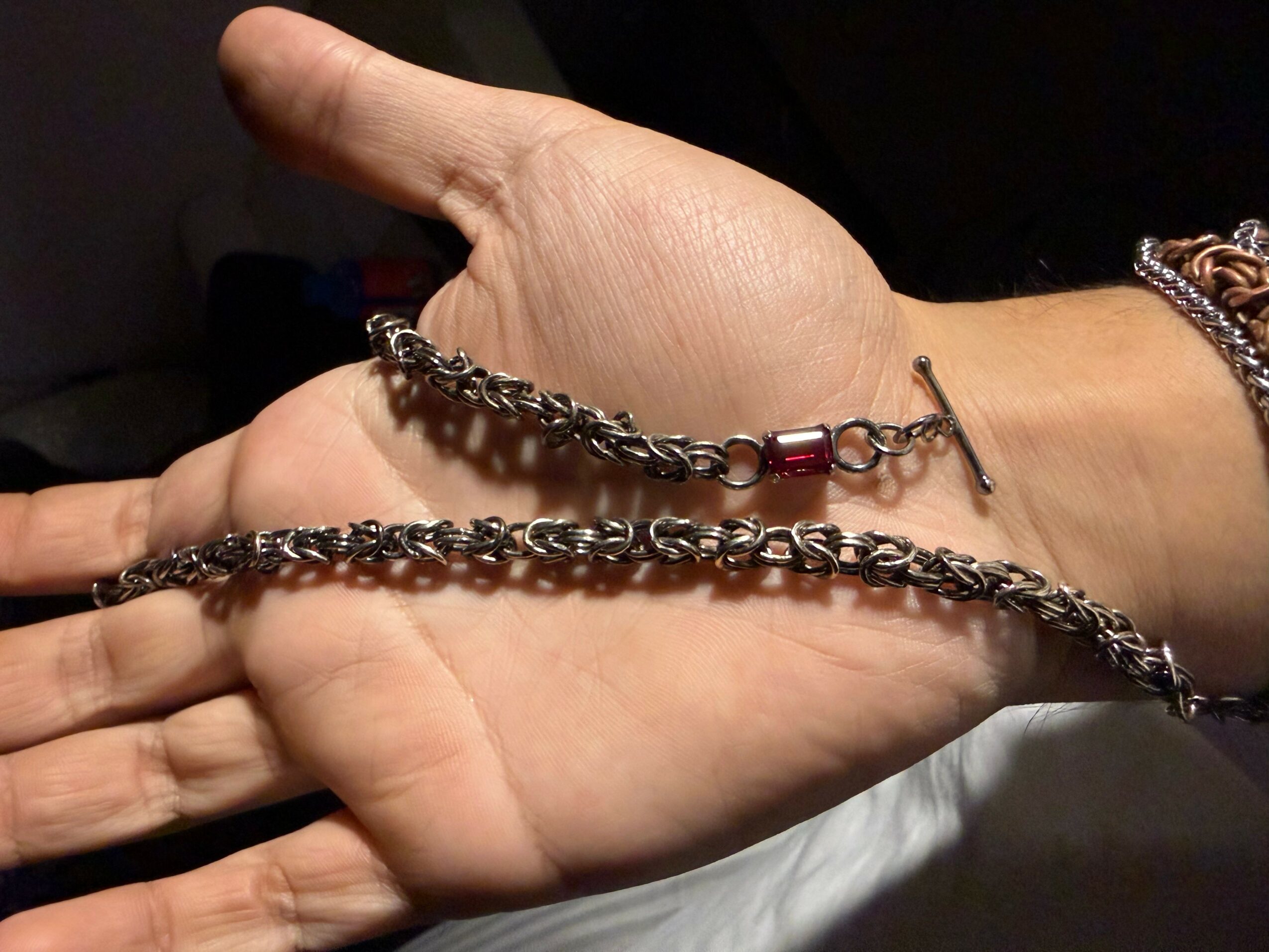 Two hands, one with a chain bracelet and a red beaded bracelet, are positioned with palms facing each other.