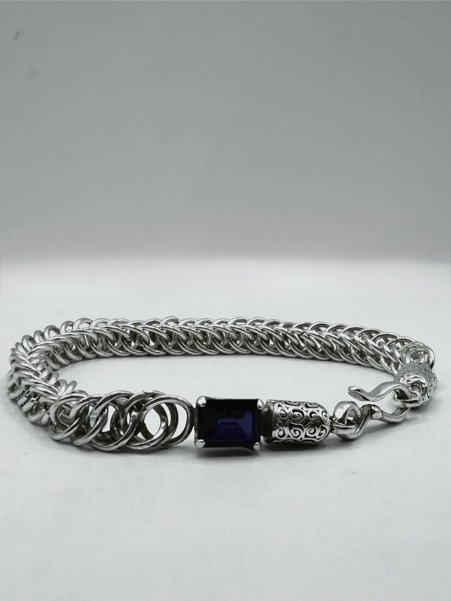 Silver chain bracelet with a dark rectangular stone and decorative metal accents, lying flat on a plain background.