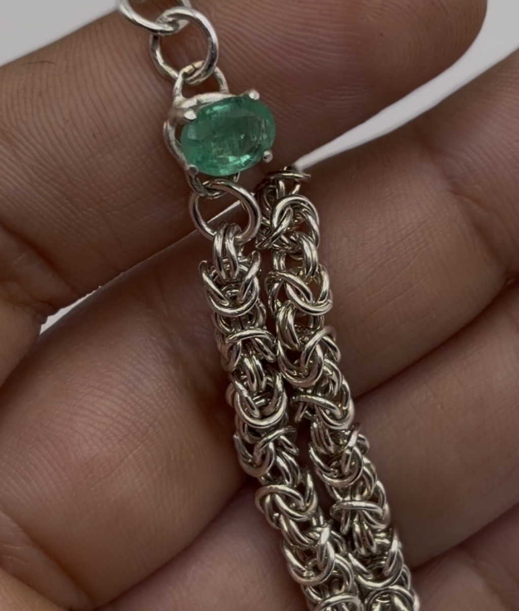Close-up of a silver chain with a green gemstone bead, held between fingers, against a neutral background.