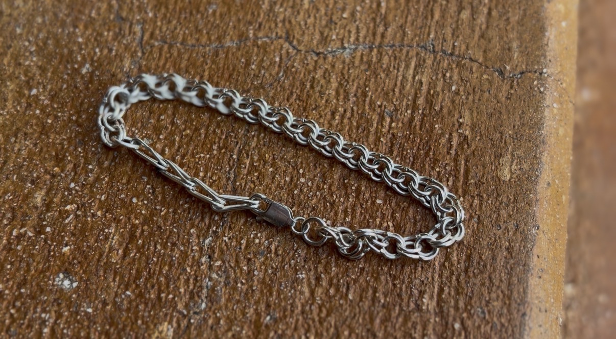 Silver chain bracelet on wooden surface, close-up view, no visible clasp, textured background.