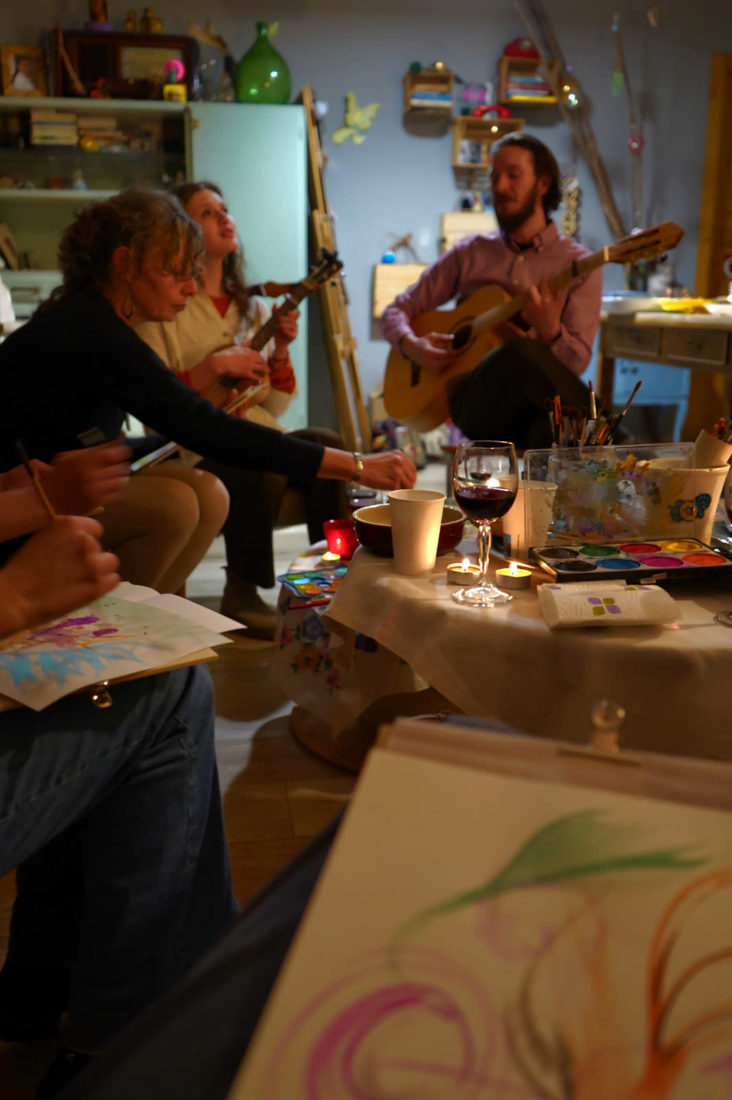 People playing guitars and singing in a cozy room with tables, drinks, and colorful decorations.
