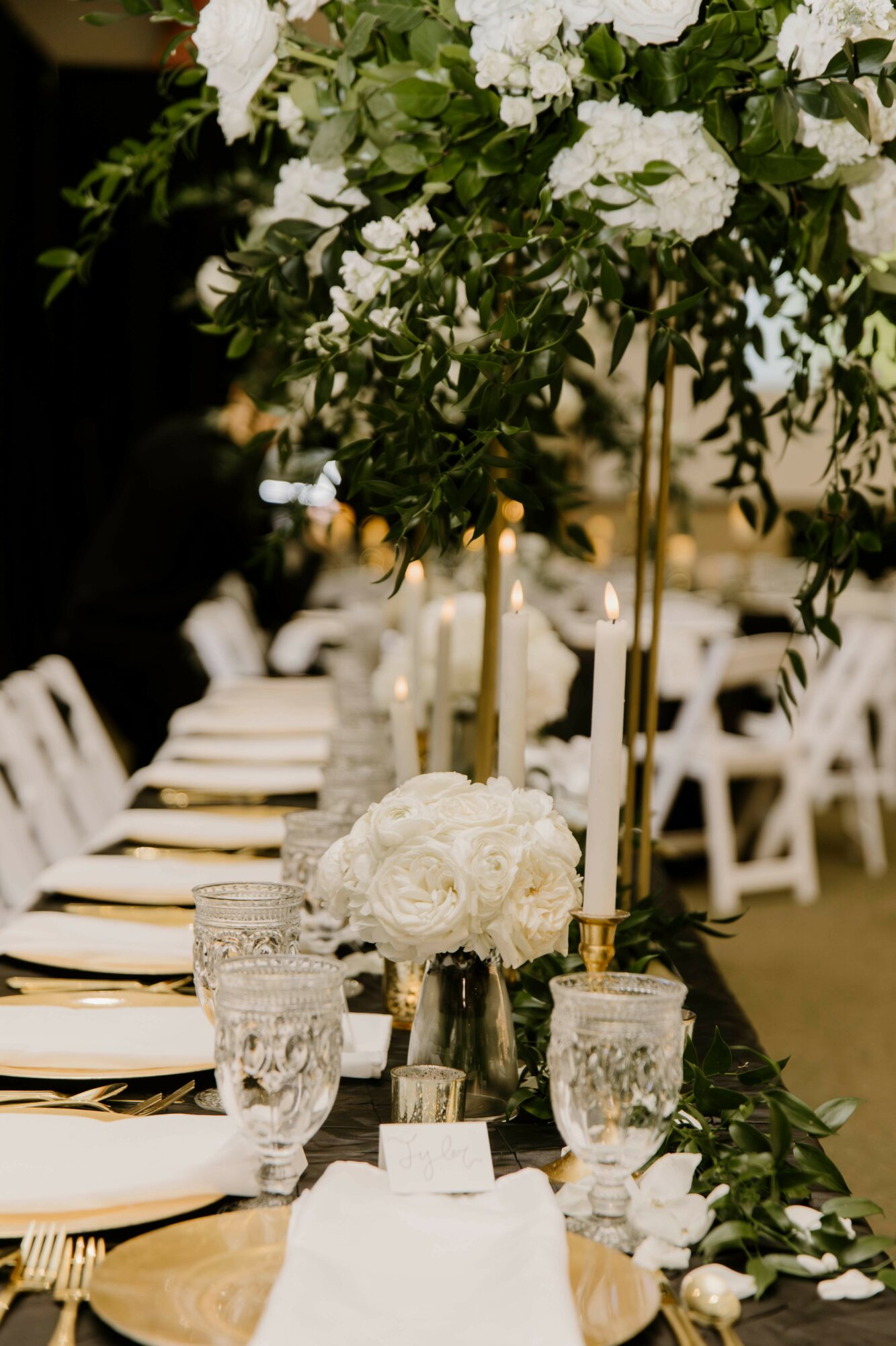 Elegant table setting with white floral centerpiece, tall floral arrangements, and place settings with glasses and cutlery, in a decorated event space.