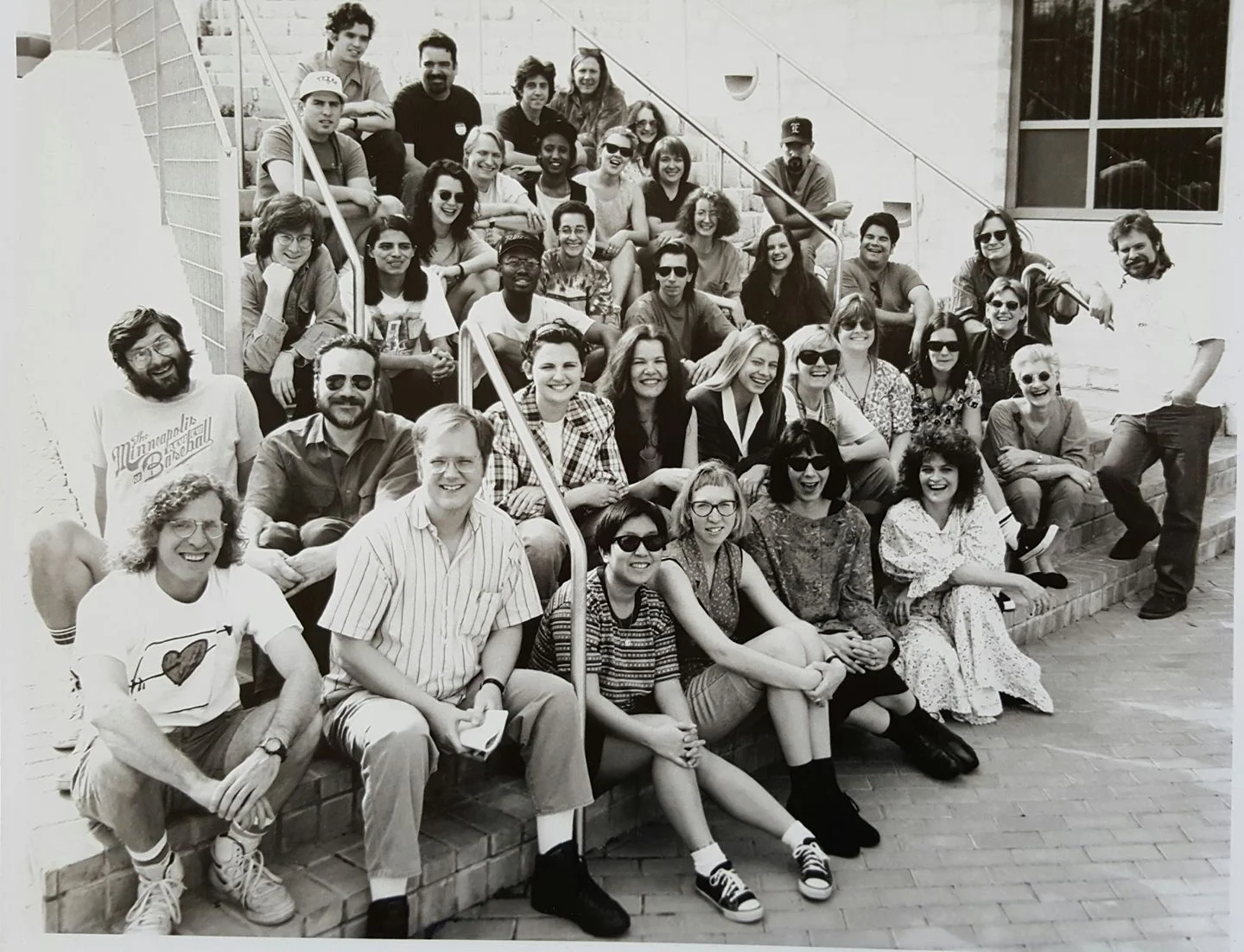 Group of people sitting and standing on outdoor stairs, smiling, in black and white photo.