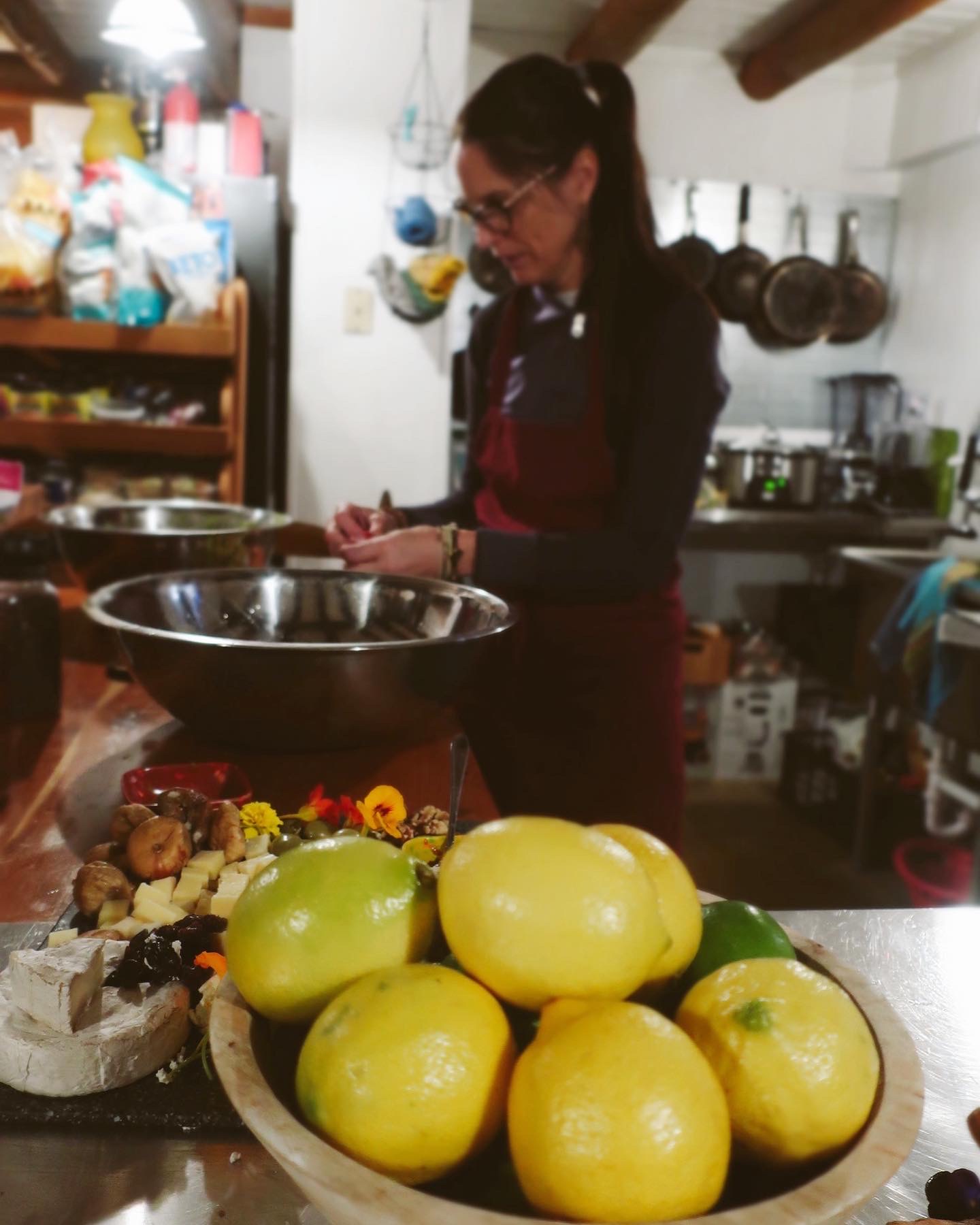 Person in kitchen preparing food, with a bowl of yellow fruits and other ingredients on the counter.