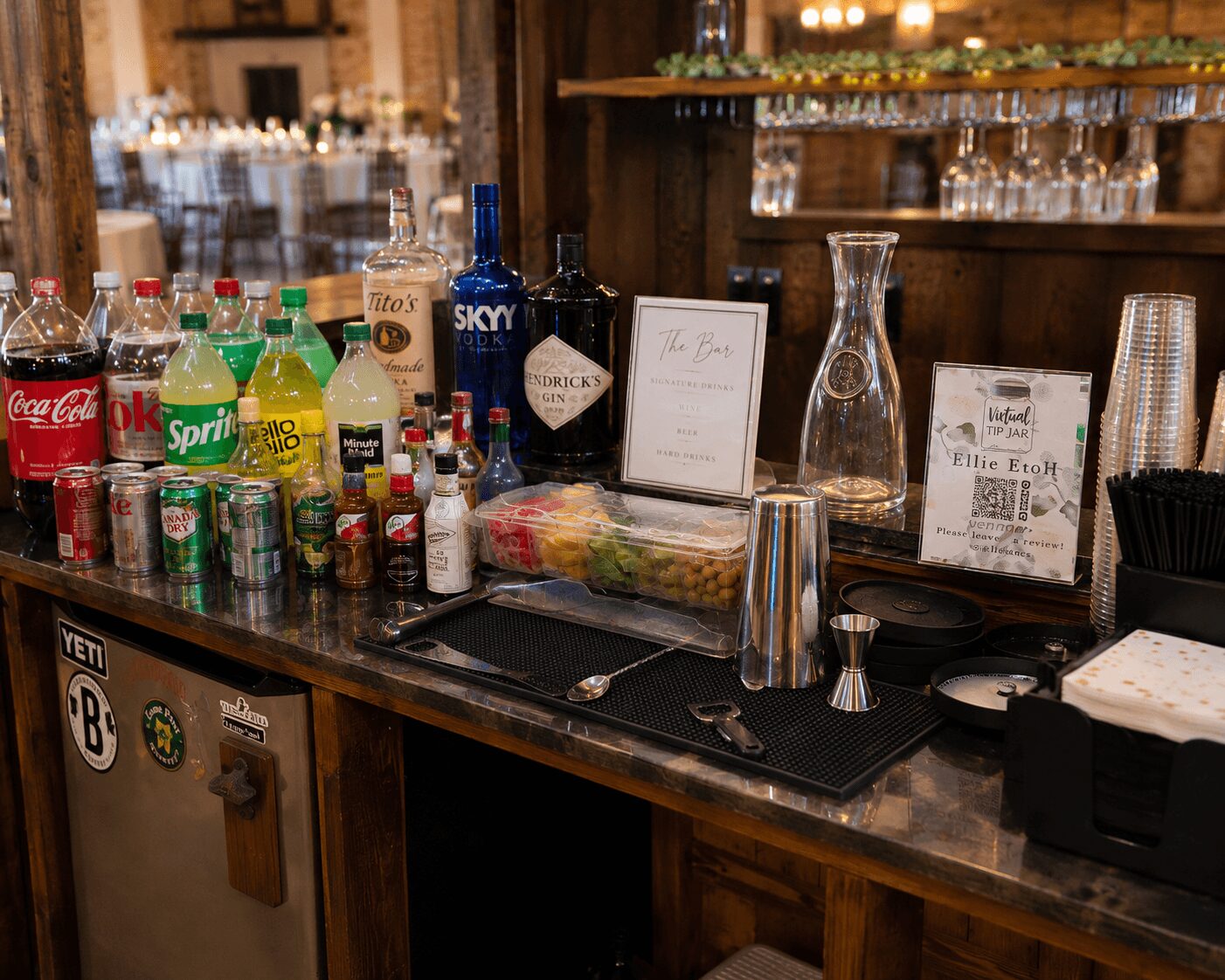 Bar counter with bottles of soda, alcohol, glasses, and bar tools in a restaurant setting.