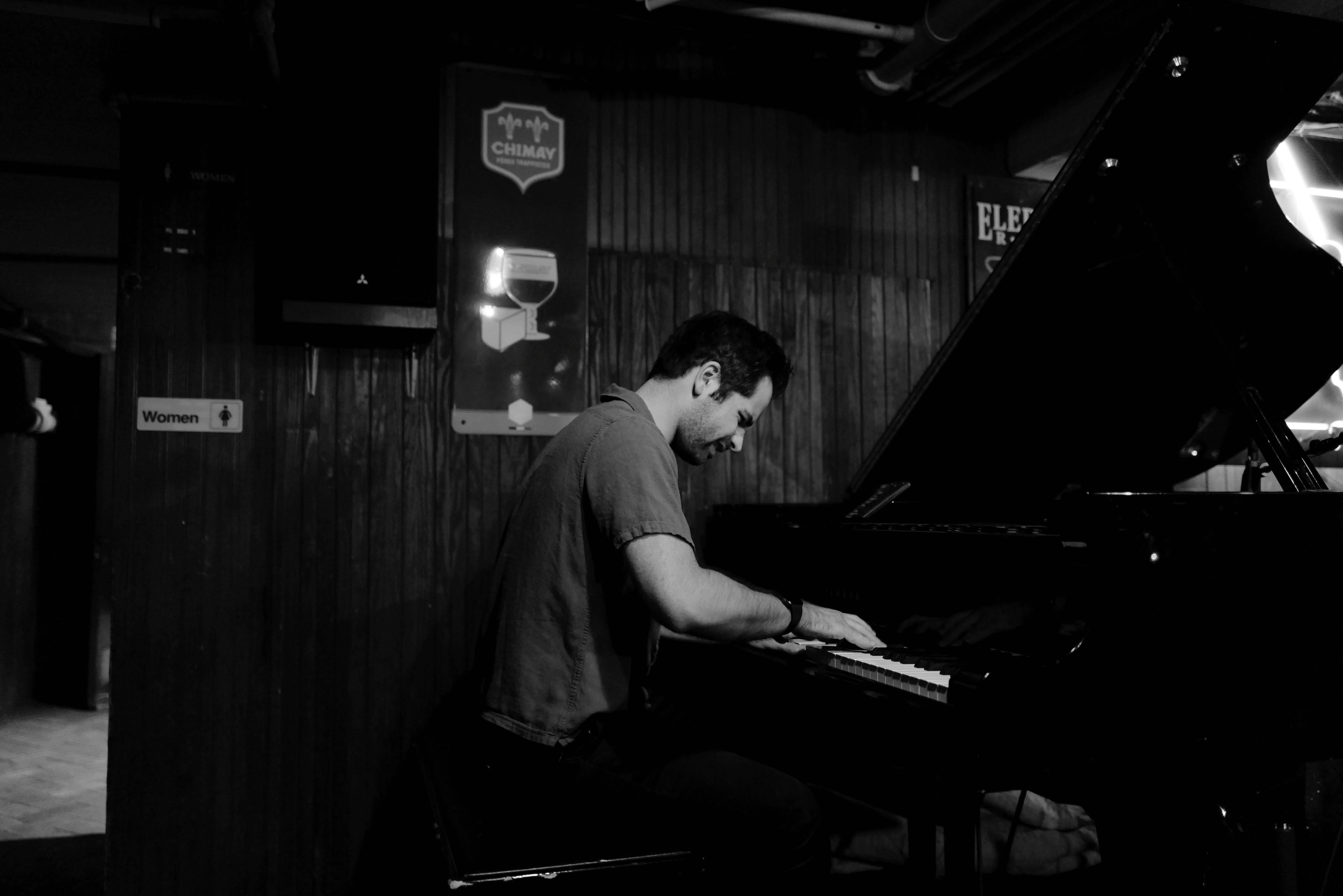 Person playing piano in a dimly lit room with wooden walls, focused on the keys.