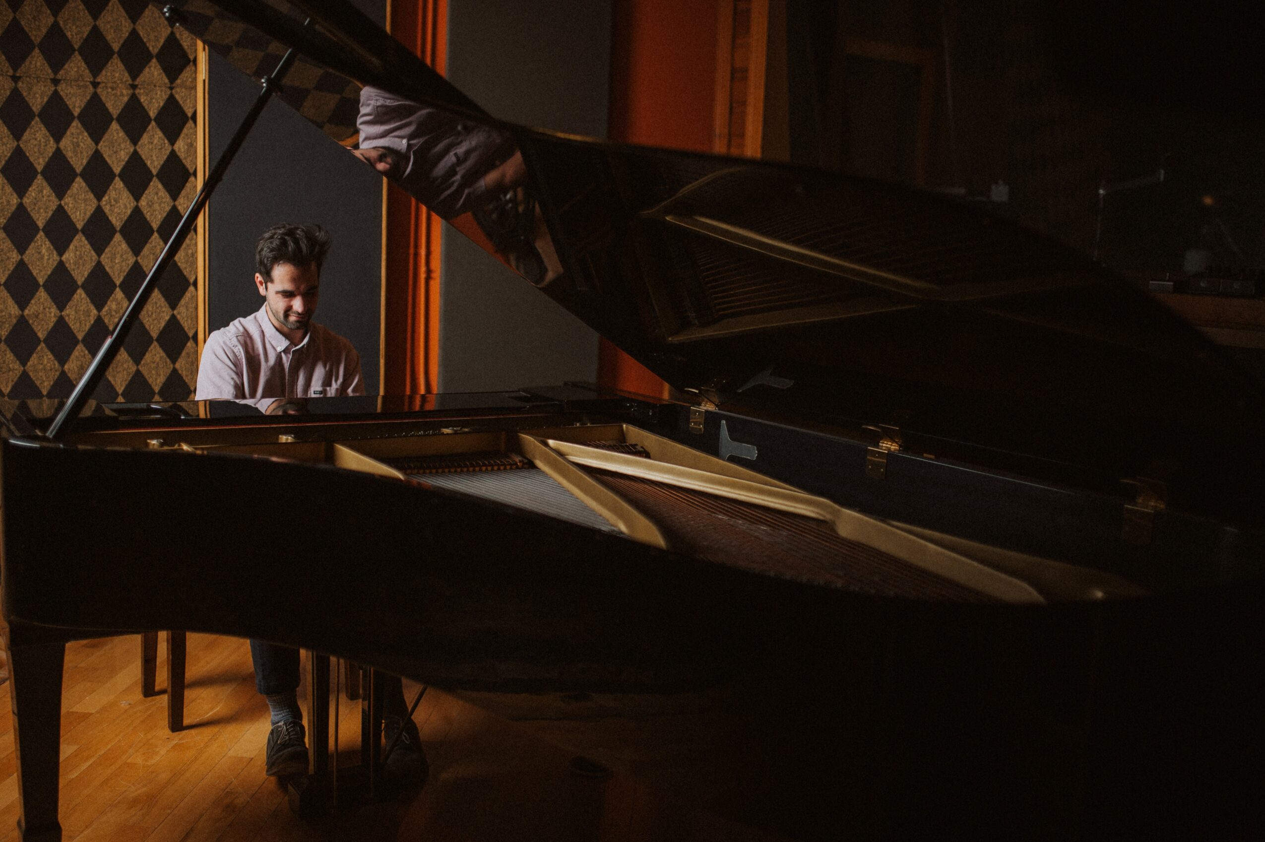 Person playing piano in a dimly lit room with soundproofing panels, reflected on the open piano lid.