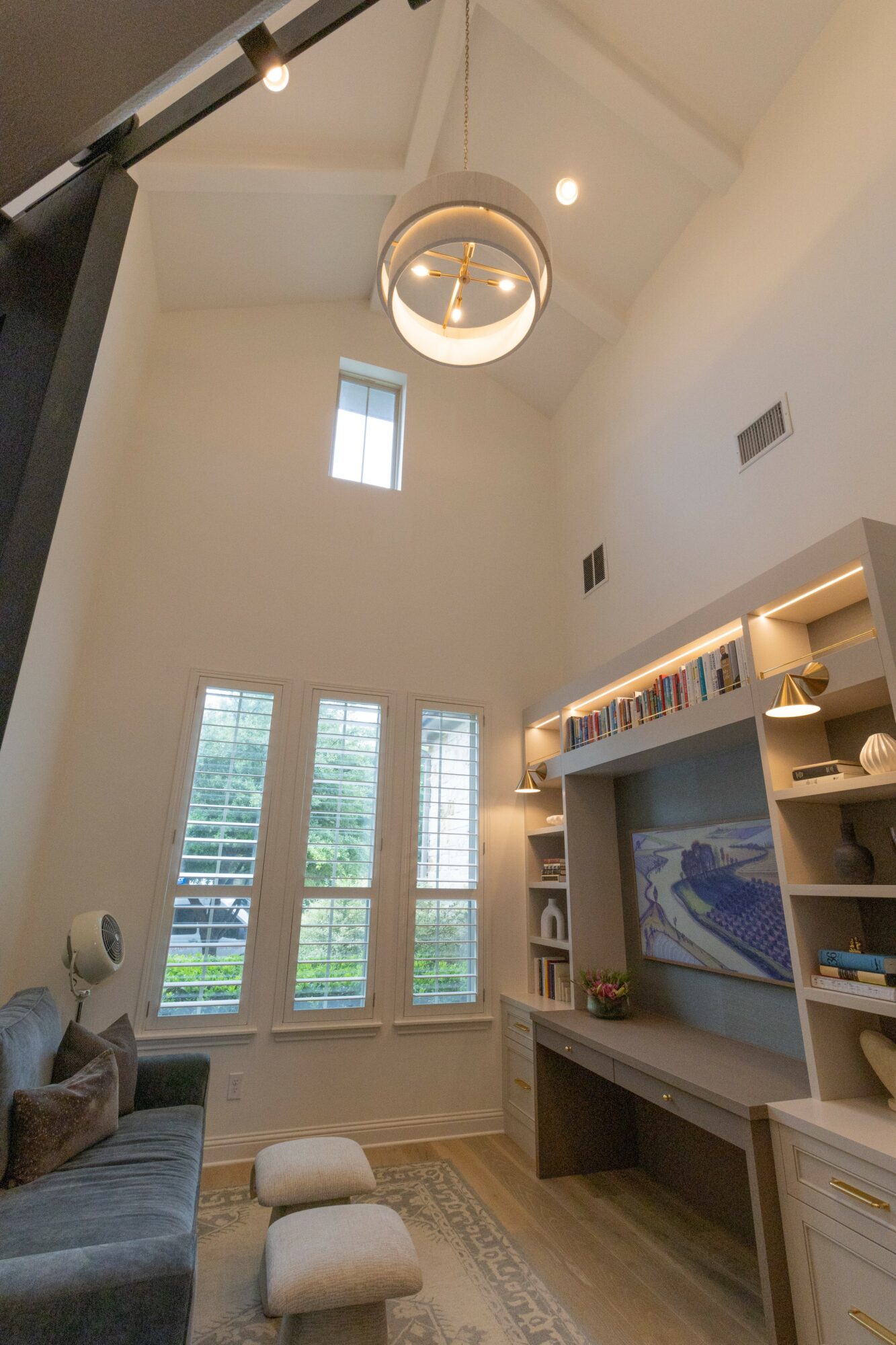 Living room with high ceiling, large windows, a wall-mounted TV, and built-in shelves, illuminated by a modern ceiling light.