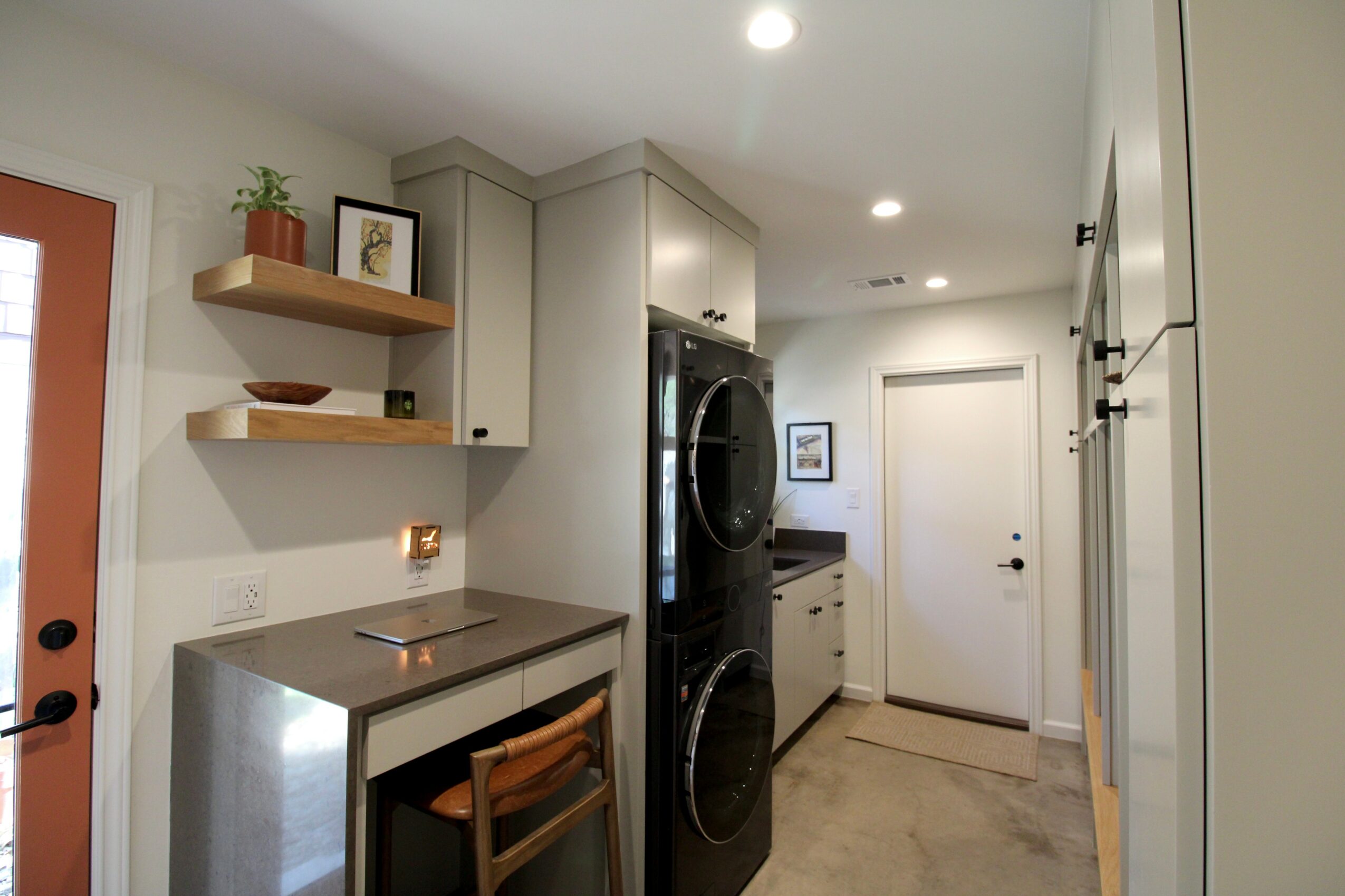 Kitchen with stacked washer and dryer, cabinets, and open shelves, viewed from the doorway, with a door at the end.