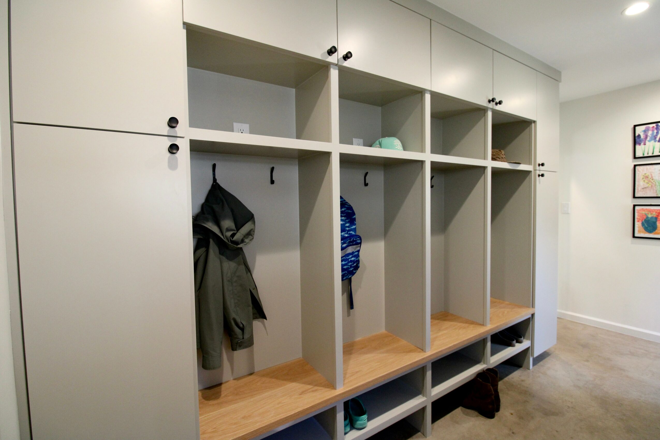 Open storage lockers with hooks and shelves, some with clothing and items inside, in a room with wall art.