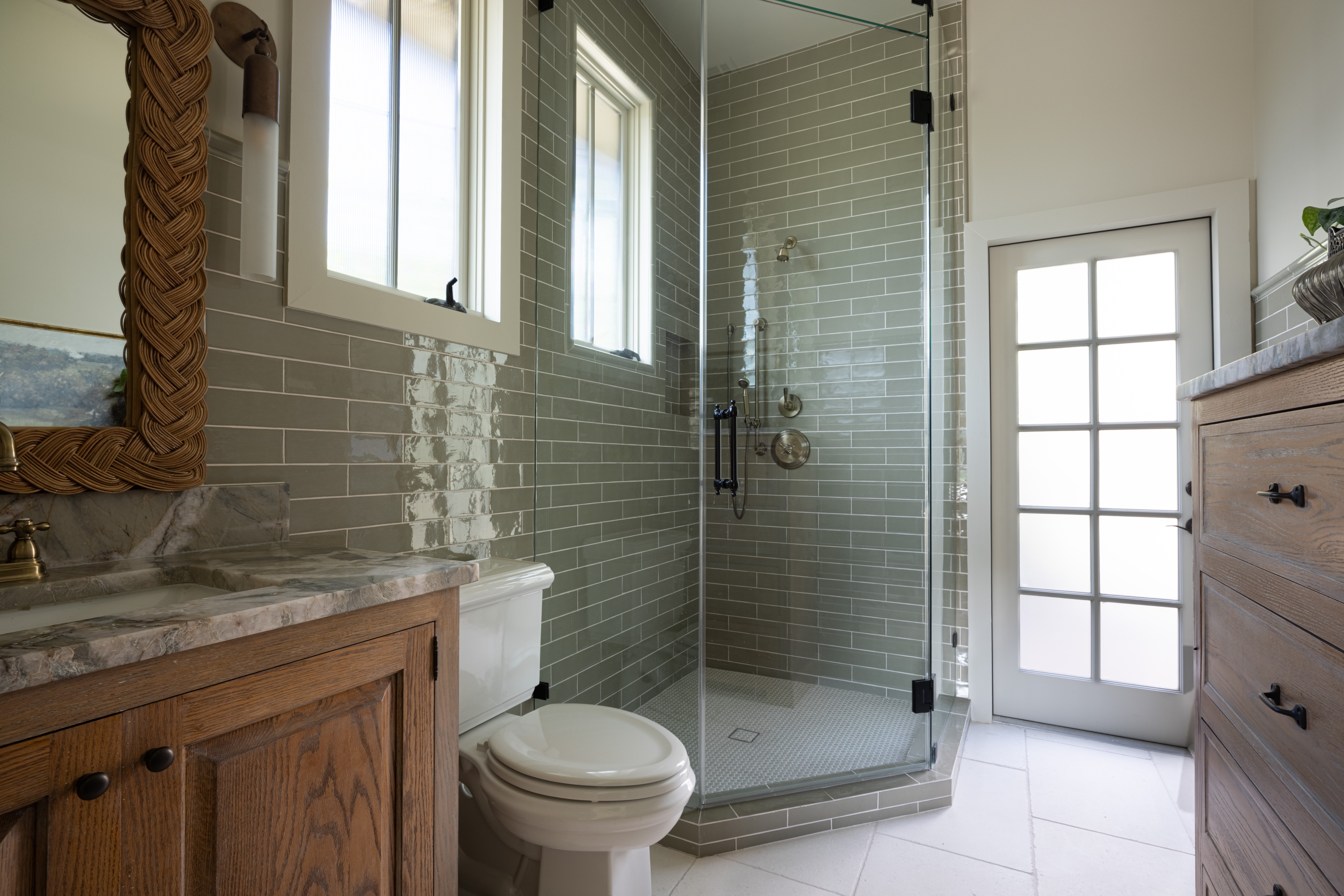Bathroom with shower, toilet, wooden cabinet, and door with window, tiled walls and floor, and a mirror.
