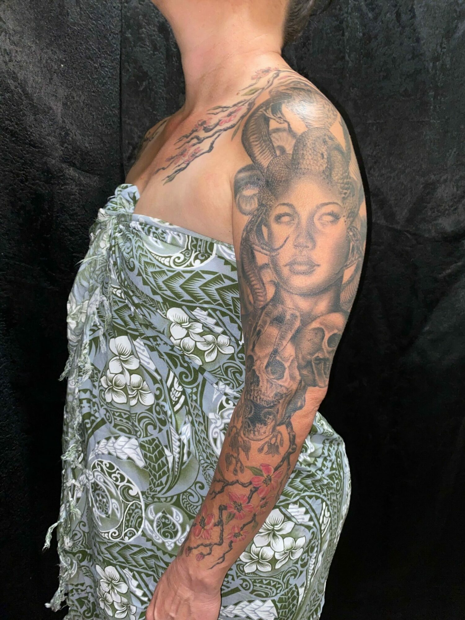 Person with tattoos on arm and shoulder, wearing patterned pants, lying on a dark surface.