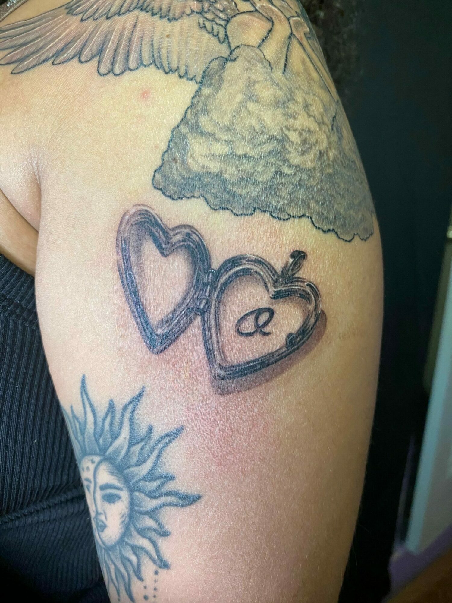 Tattoo of two open heart lockets, clouds, and a sun with a face on skin.