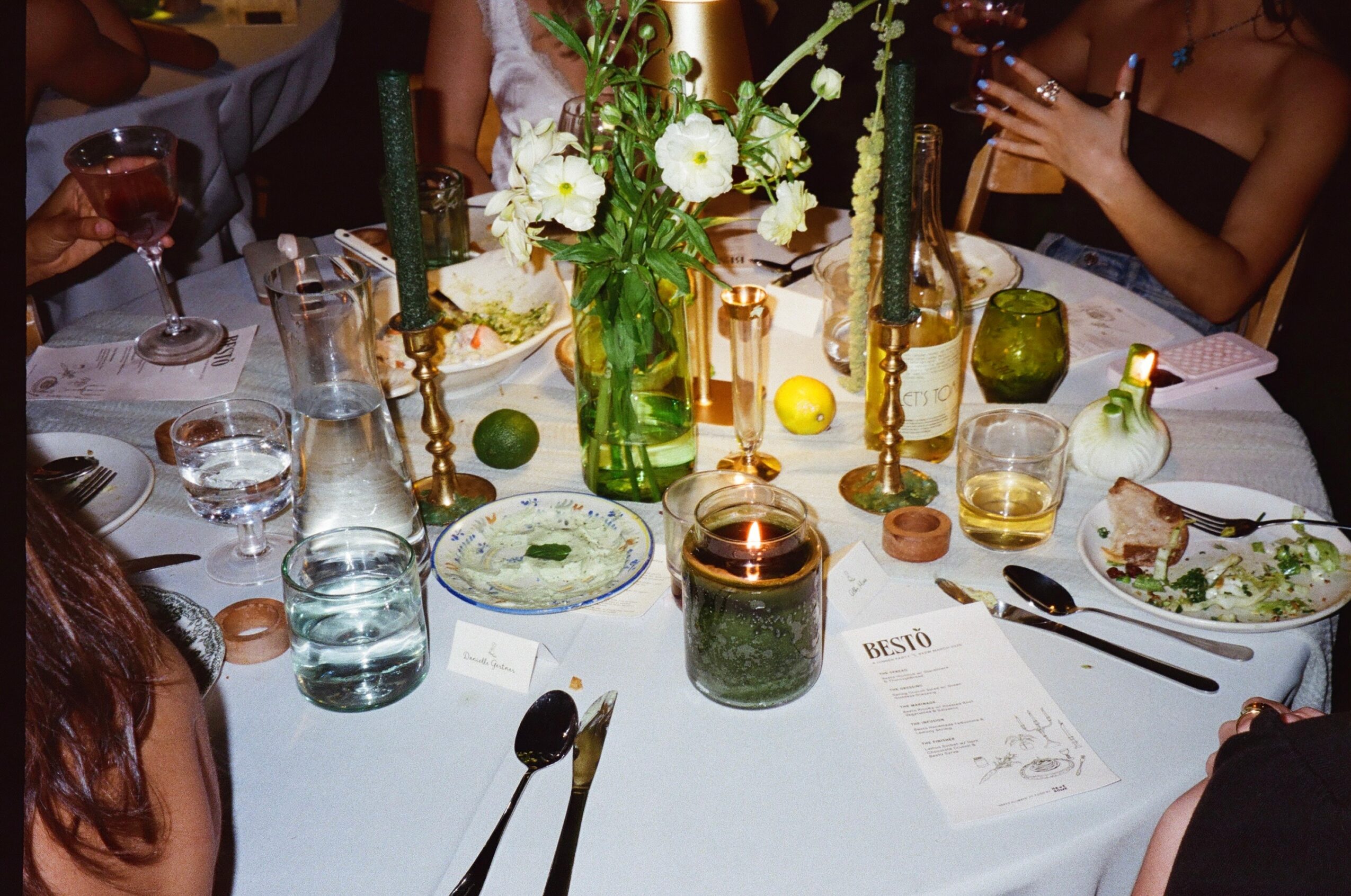 Table with floral centerpiece, candles, drinks, and place settings at a social gathering.