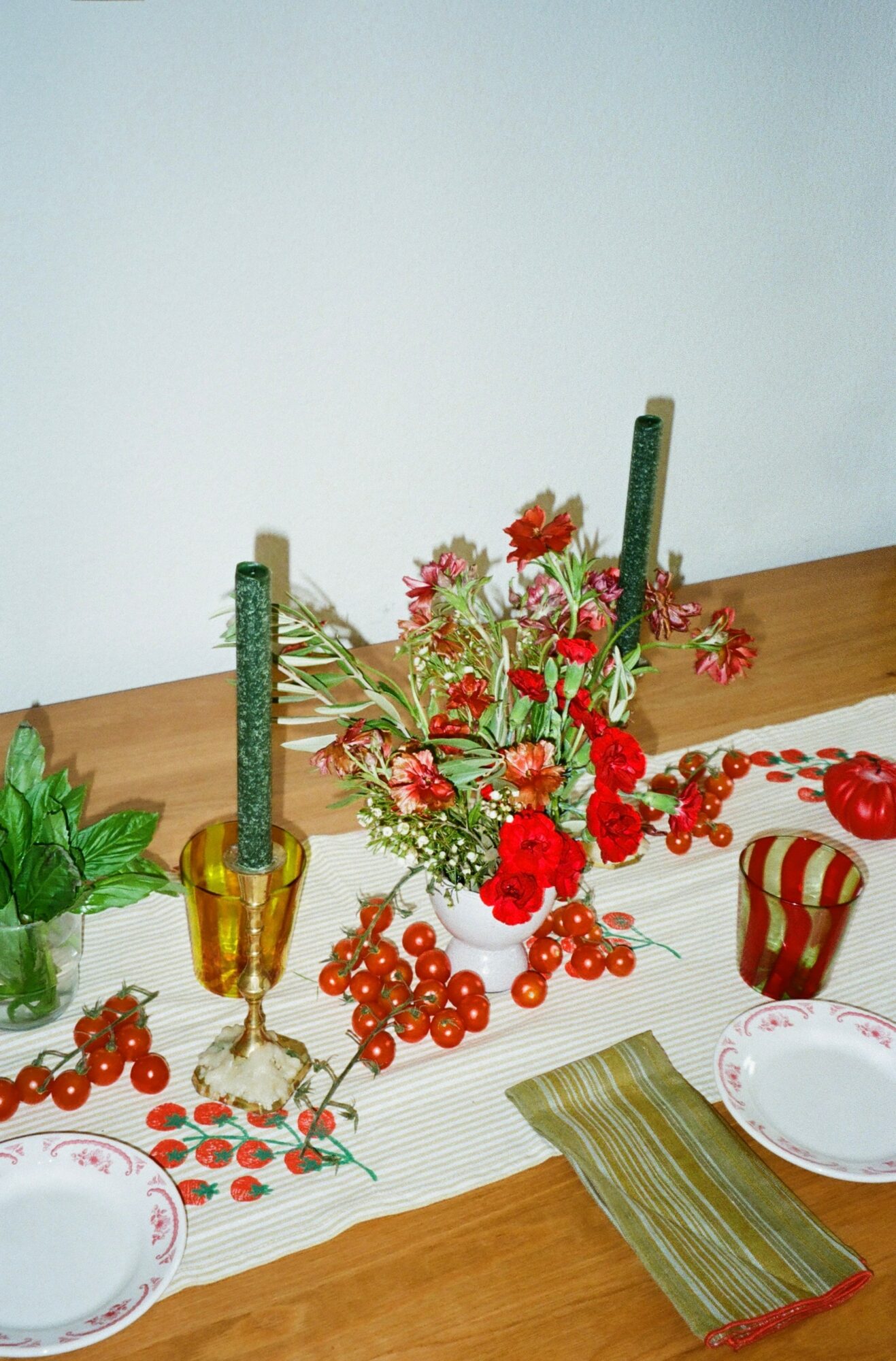 Flower arrangement with red and white flowers, green candles, and decorative items on a table, with plates and a napkin.