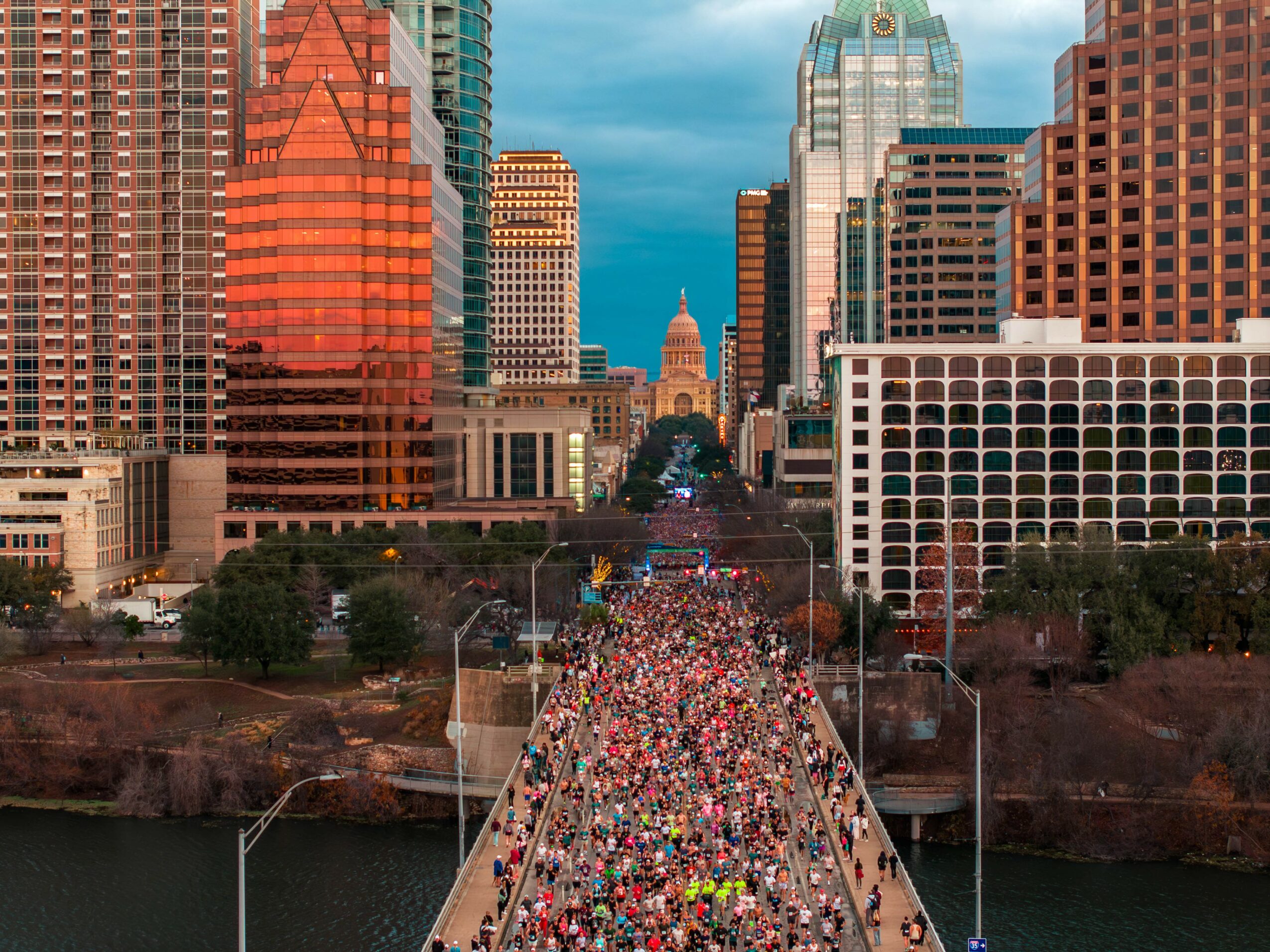 City skyline with tall buildings and a large crowd walking on a bridge over a river.