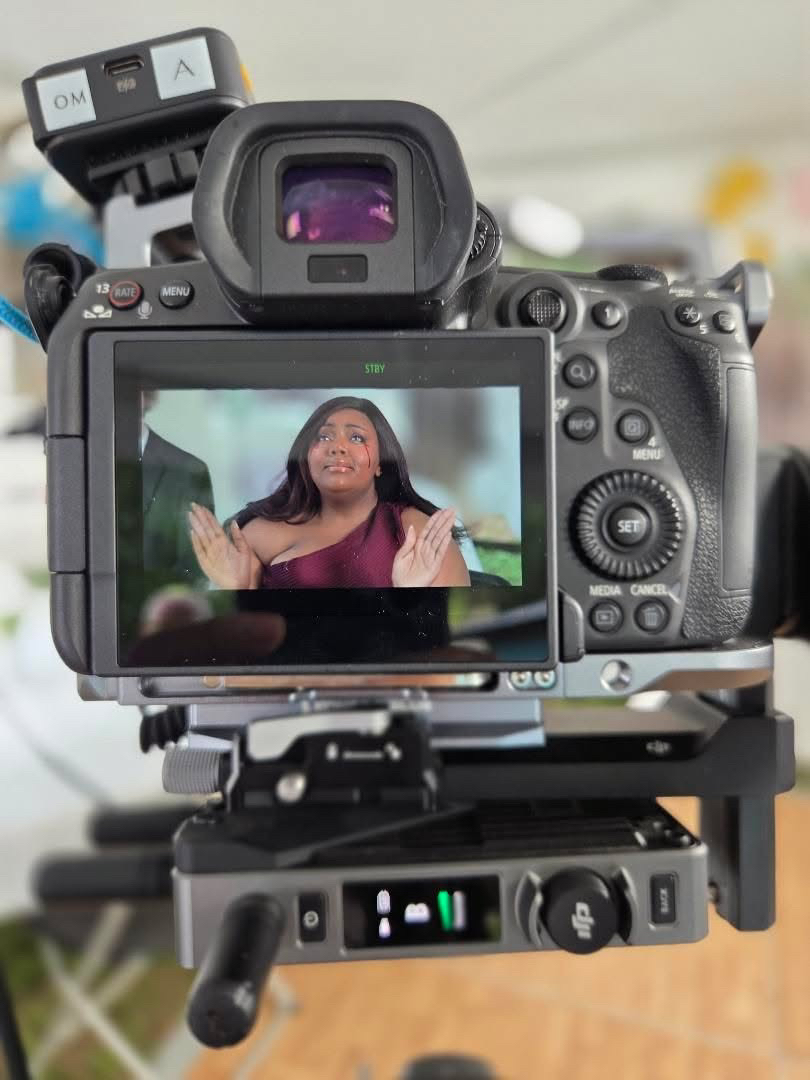 Camera capturing a woman speaking with hands raised, displayed on camera screen, in a room with blurred background.