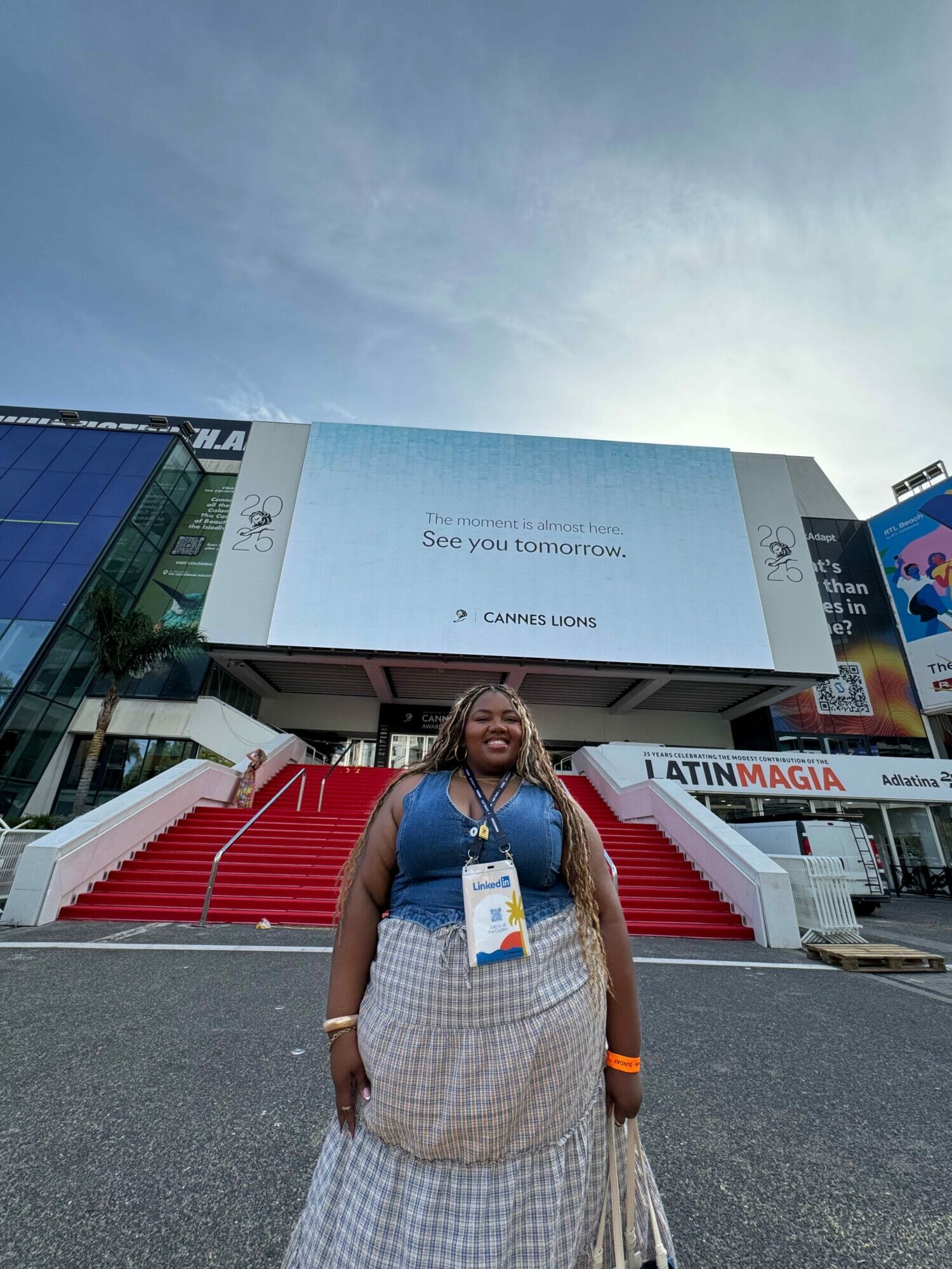 Woman standing outside a building with a large digital screen, red stairs, and a blue sky.