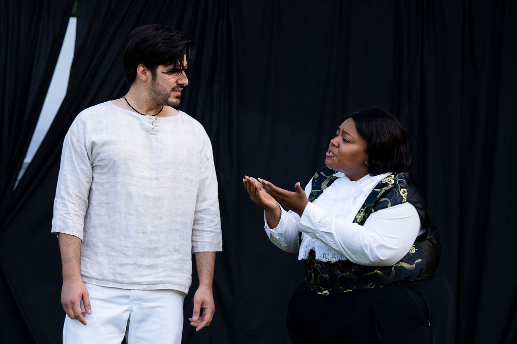 Two people engaged in conversation, one holding an object, against a dark background.