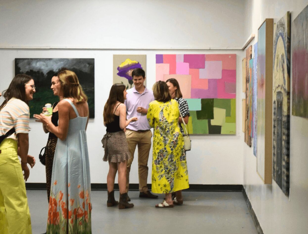 Group of people talking and viewing colorful abstract paintings in an art gallery.
