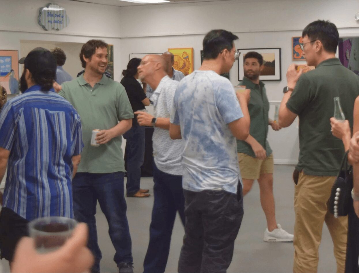 Group of people socializing in an art gallery, some holding drinks, with artwork on the walls.