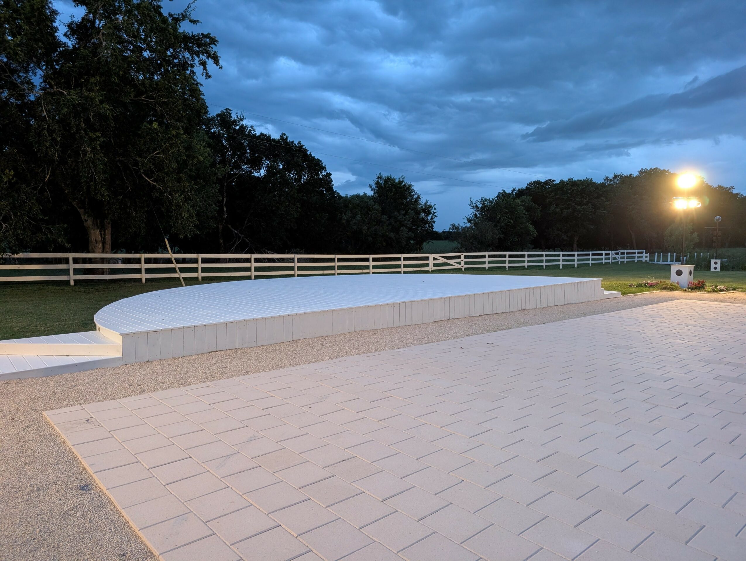 Concrete bench with a curved backrest in an outdoor area during evening, with trees and a cloudy sky in the background.