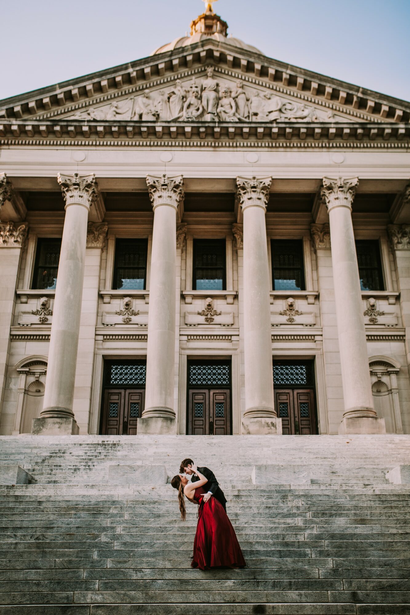 Couple dancing on steps in front of a grand neoclassical building with tall columns and detailed pediment.