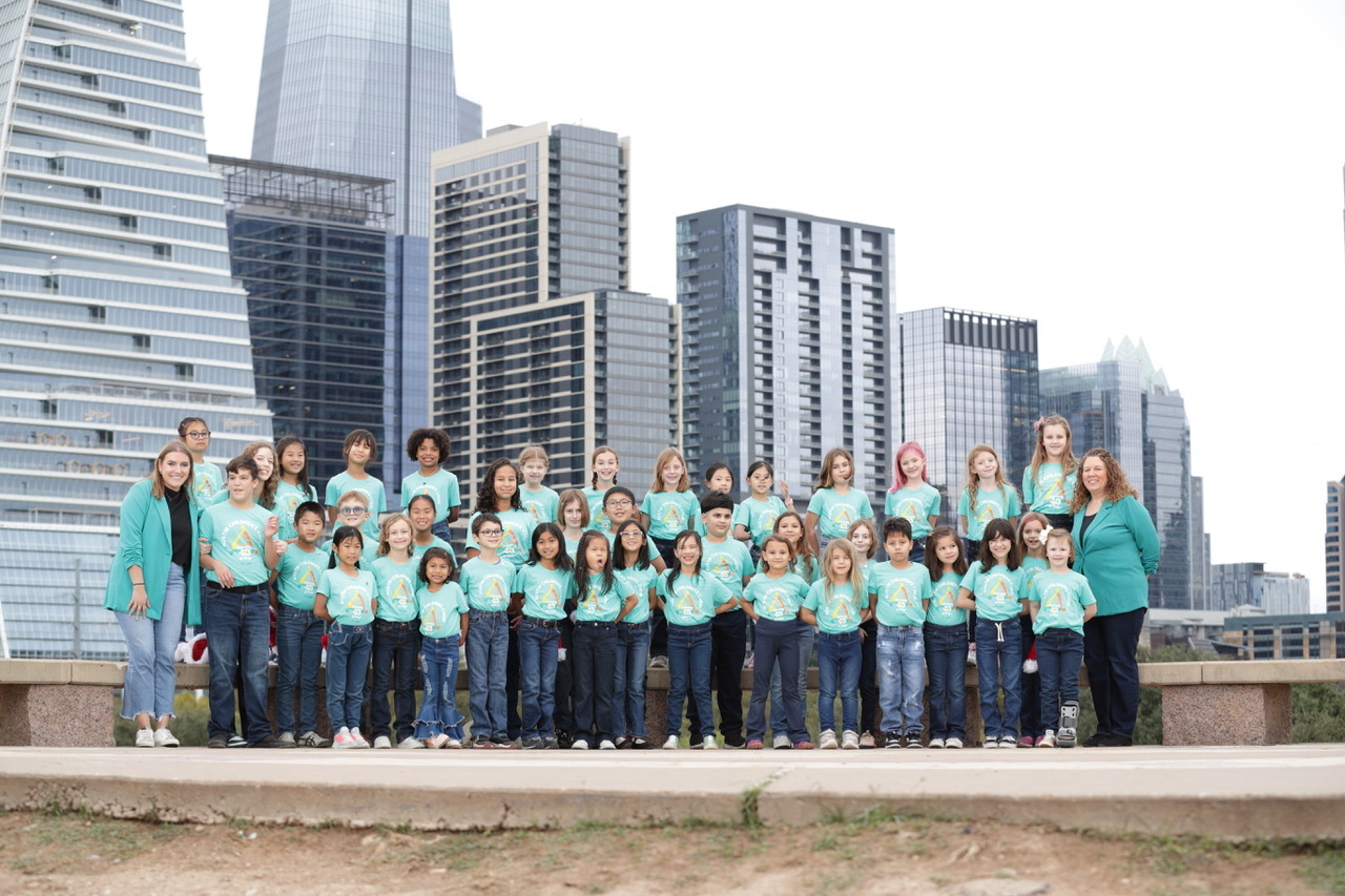 Group of children and adults standing outdoors in front of city skyscrapers, posing for a photo.