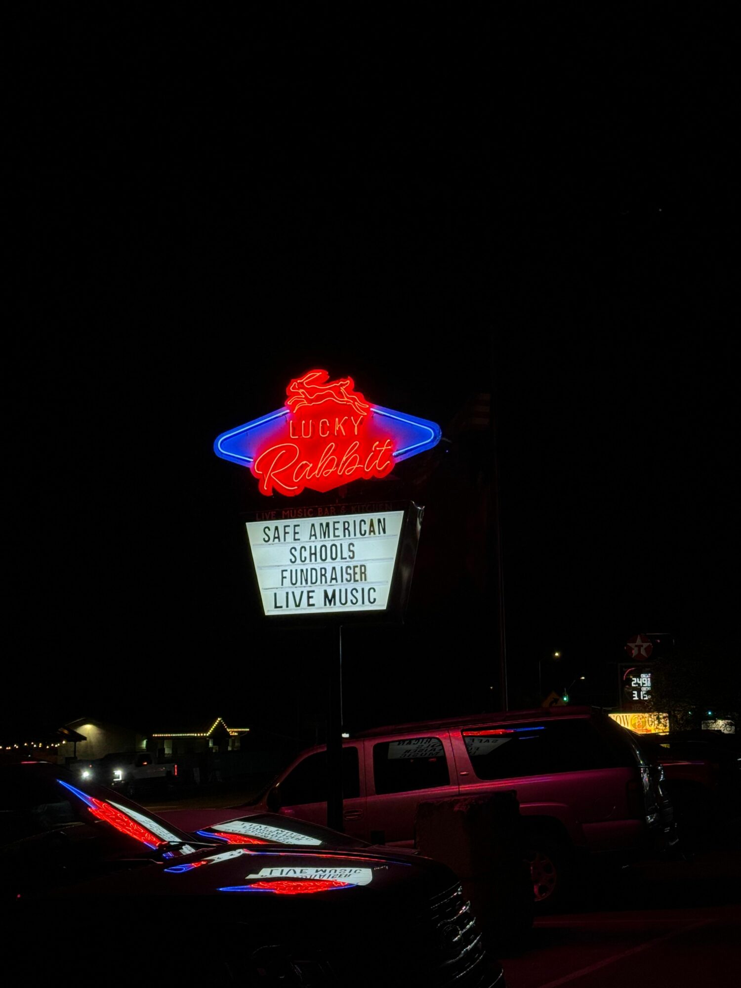 Neon sign with red and blue lights, and a white sign with black text, on a dark background.