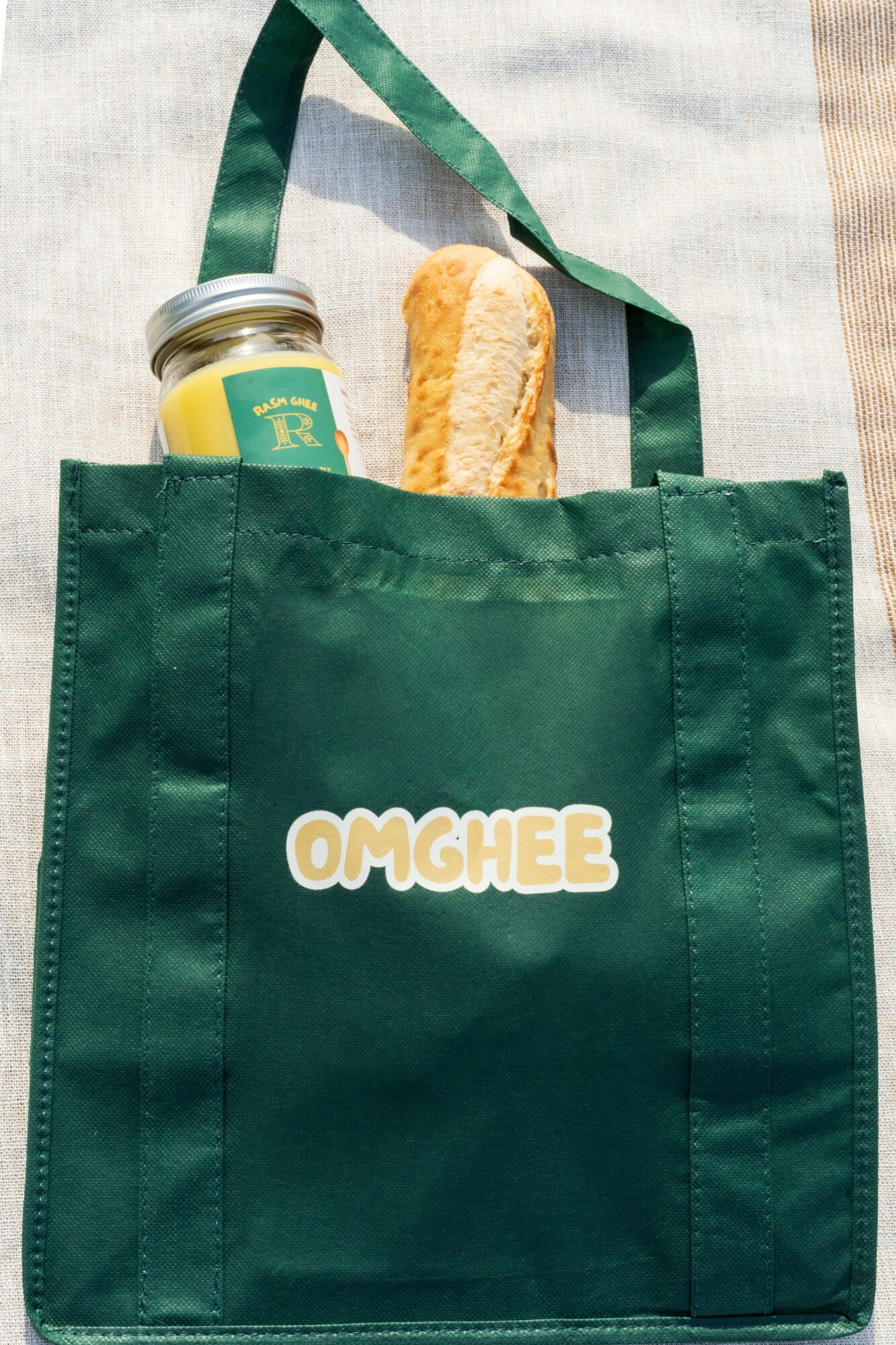 Green tote bag with a sandwich and a jar inside, on a light-colored surface, with a green strap visible.