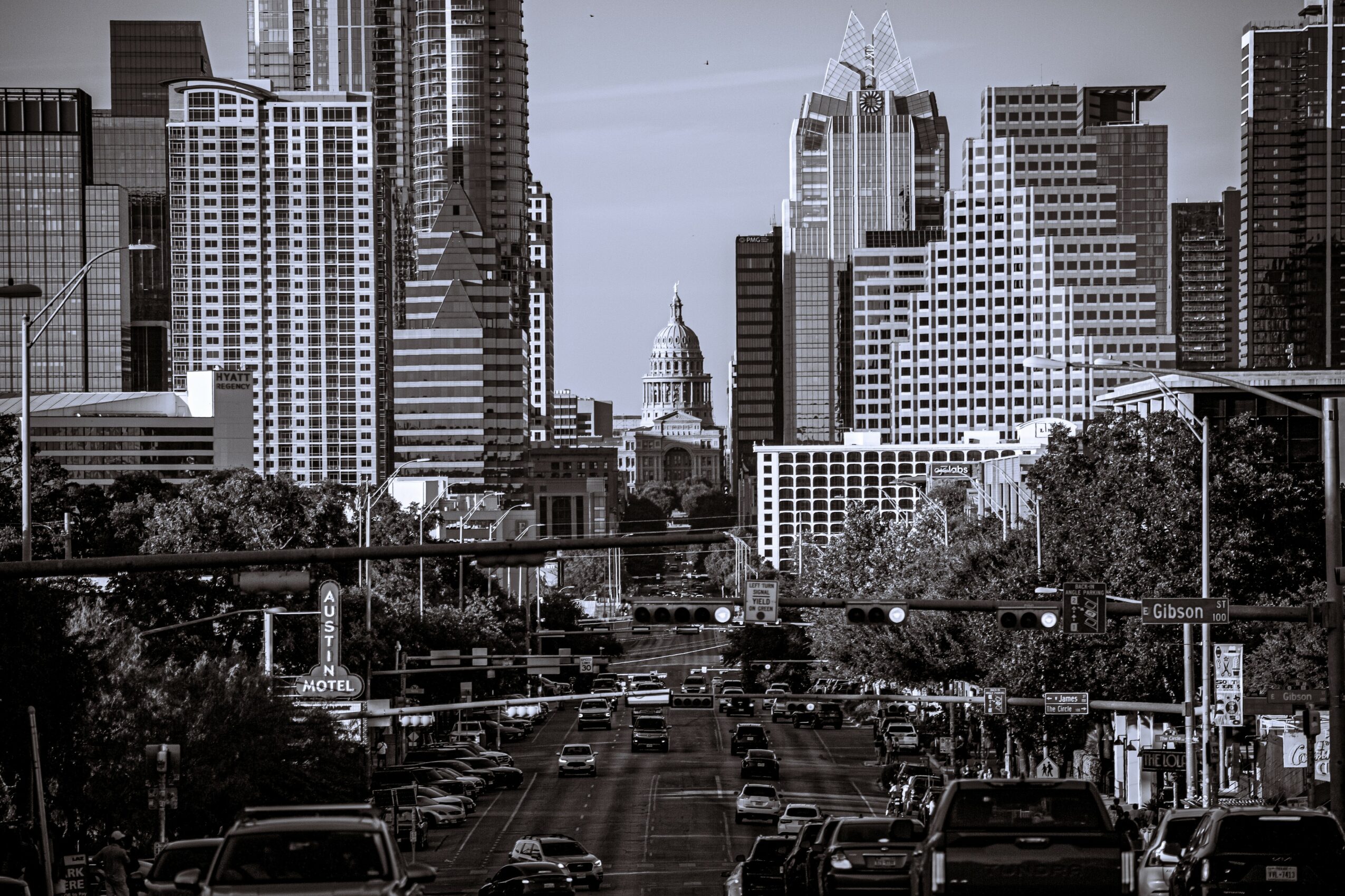 City skyline with tall buildings, busy street with cars, trees, and traffic lights.