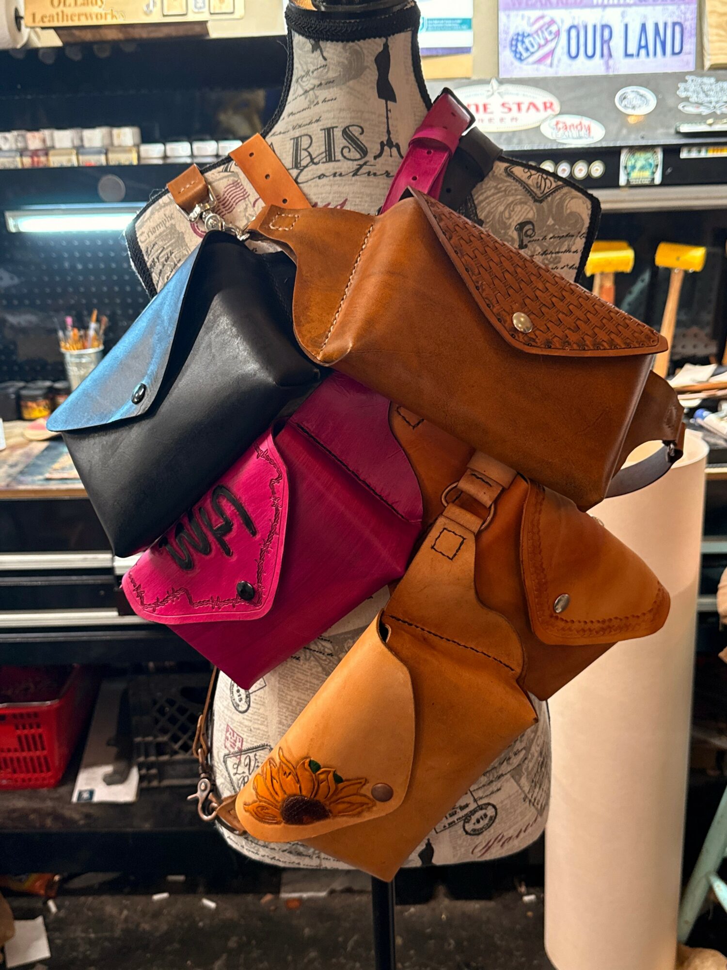 Display of various colorful handbags on a mannequin torso in a store, with shelves and signs in the background.