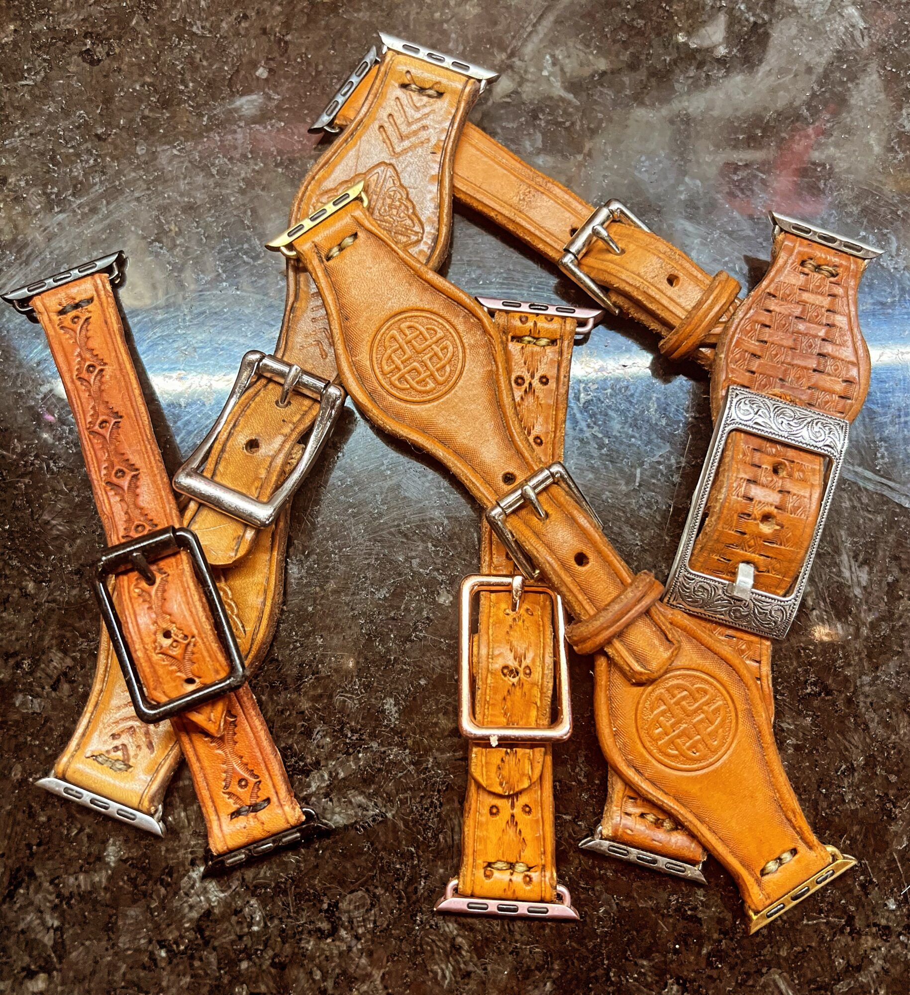 Various leather watch straps with metal buckles arranged on a dark surface.