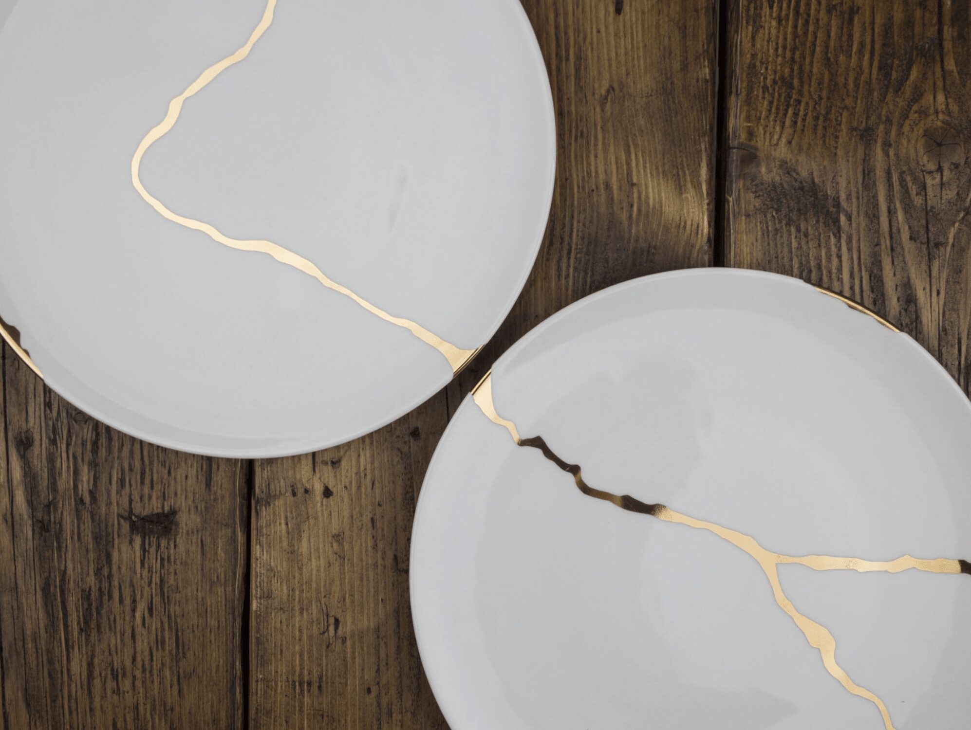 Two white plates with cracks, placed on a wooden surface.