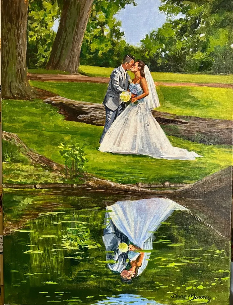 A bride and groom kiss near a pond with their reflection visible in the water, surrounded by trees and greenery.