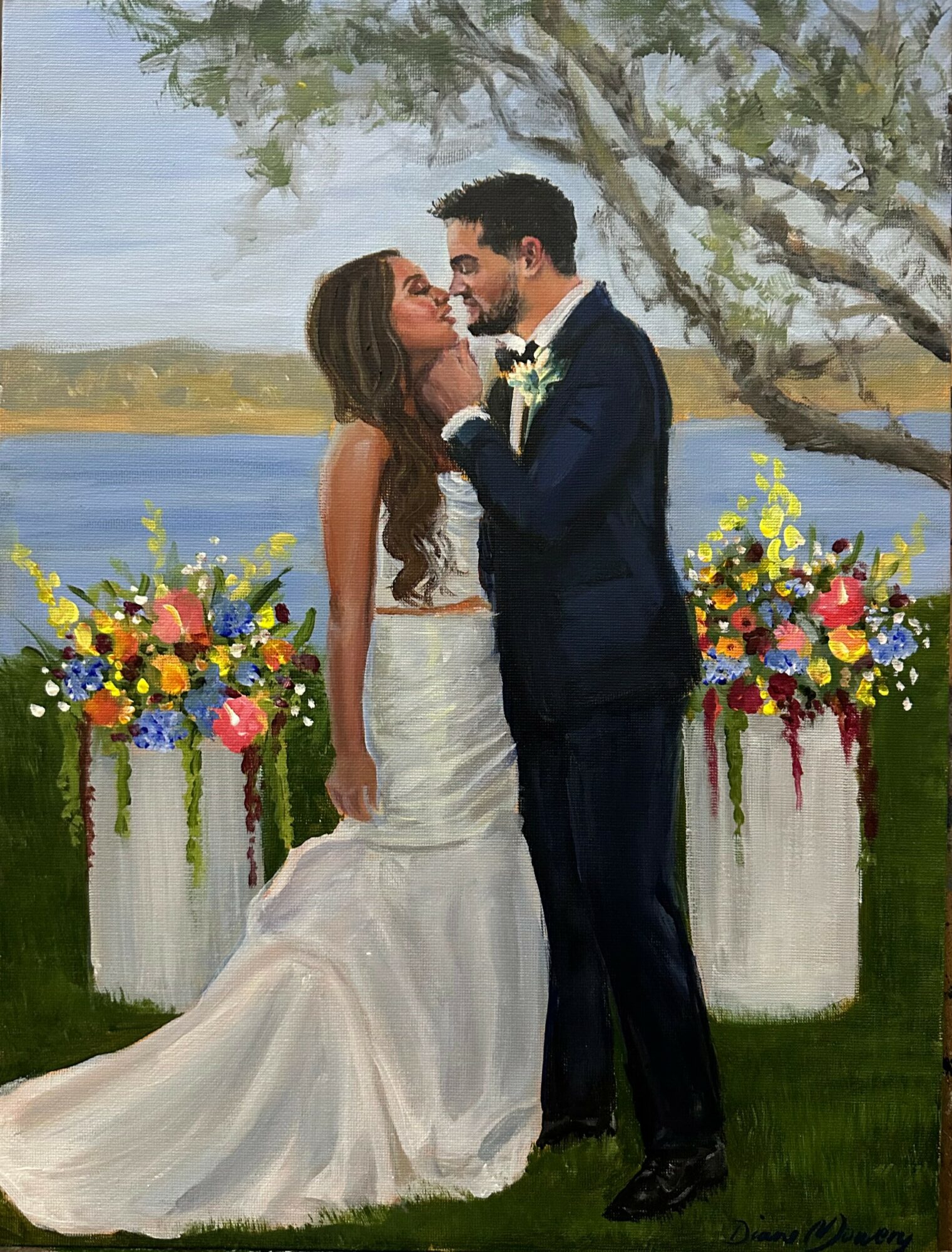 A bride and groom stand close by a lake with trees, holding hands and gazing at each other, surrounded by colorful flower arrangements.