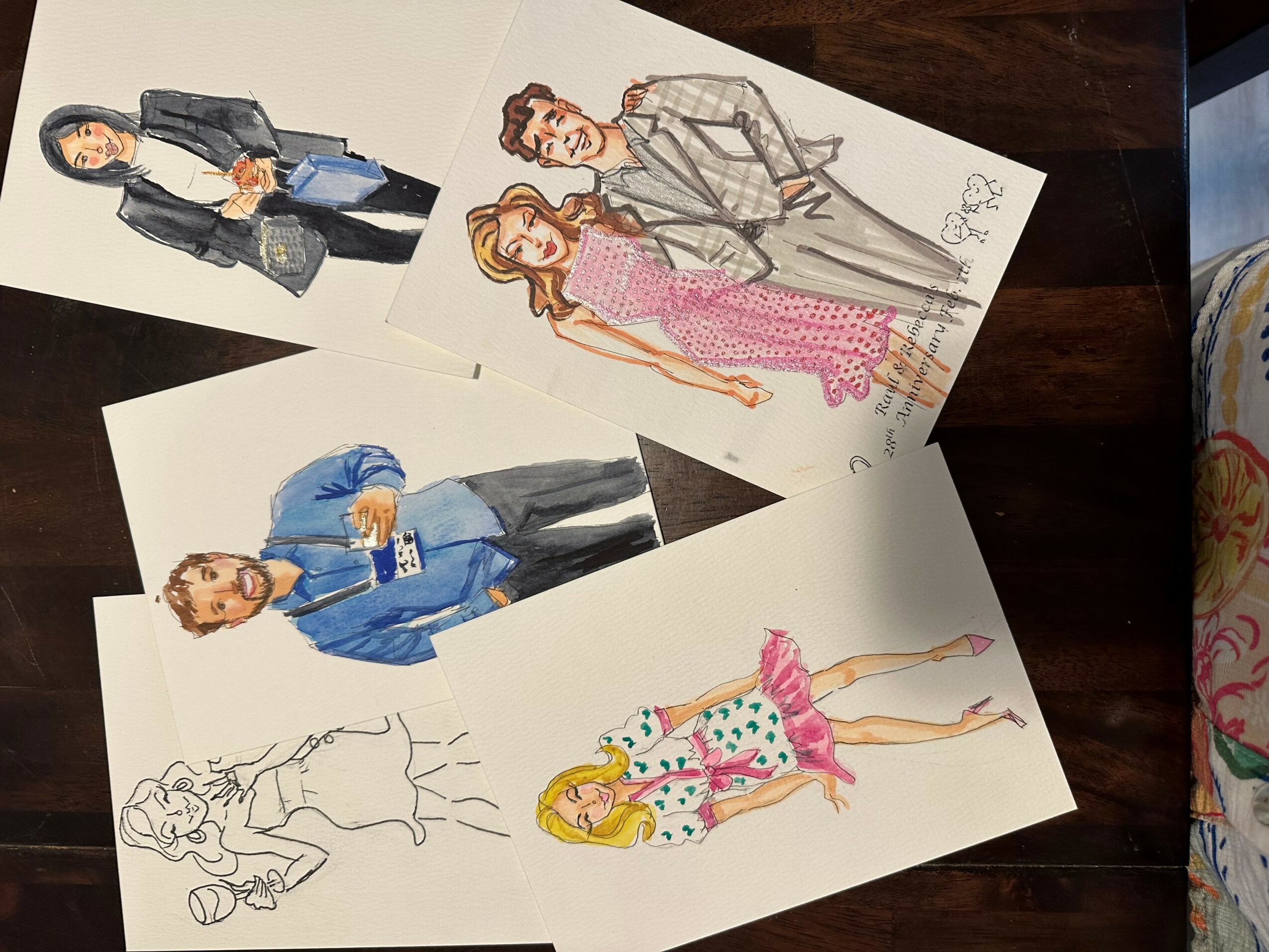 Four fashion illustrations of women in various outfits, some colored and some sketches, on a wooden surface.