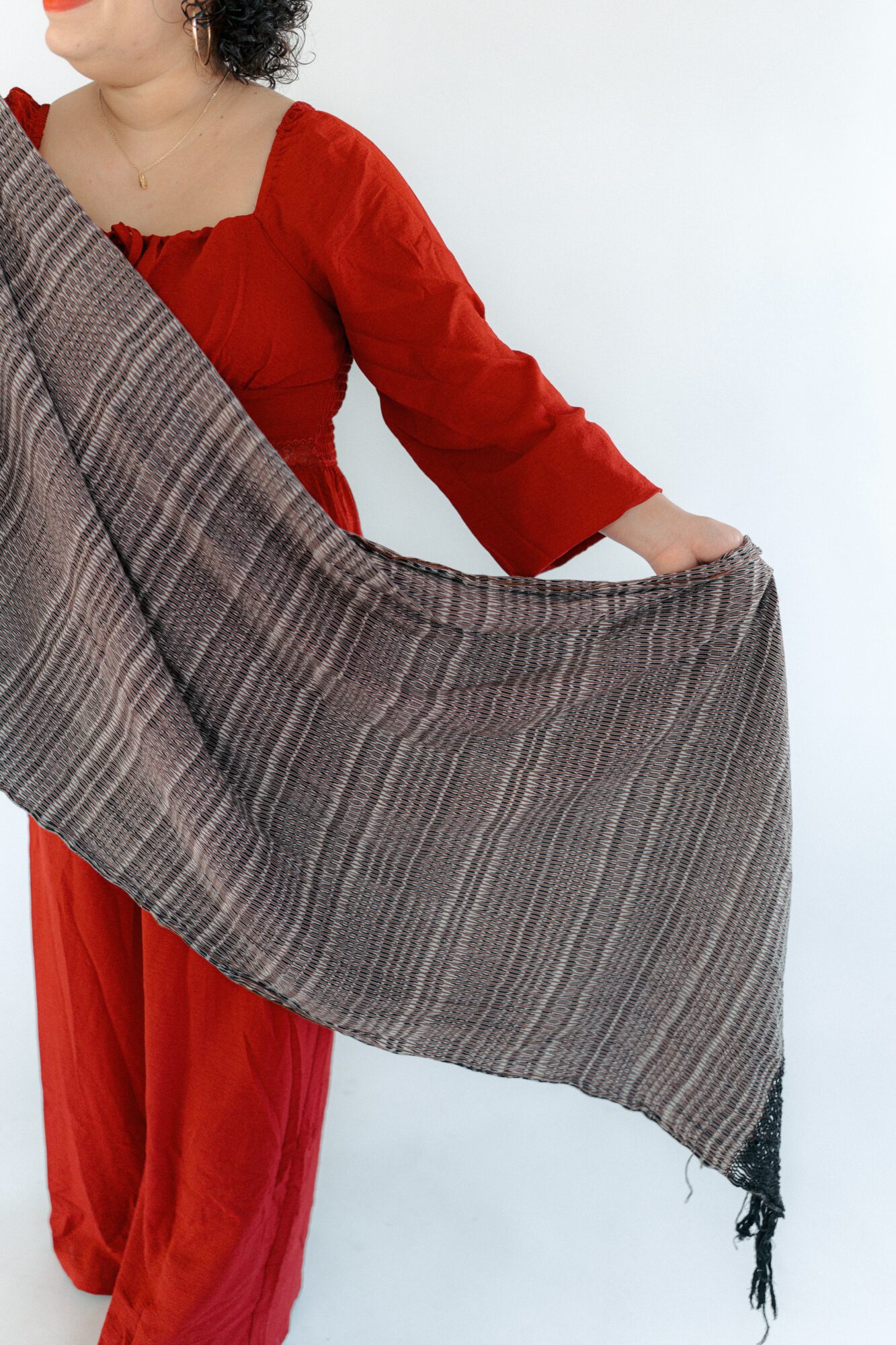 Person in red dress holding a large gray shawl, standing against a white background.