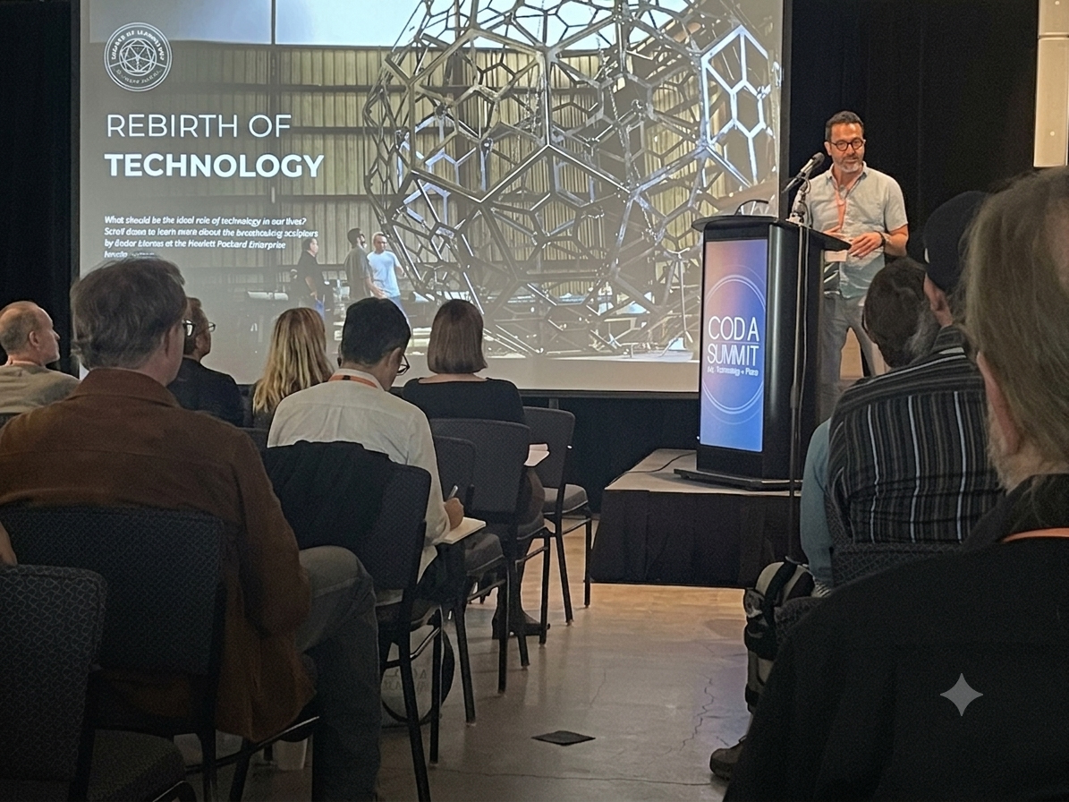 Presenter standing at a podium on stage with a large screen displaying a slide titled 'Rebirth of Technology' and a geometric background, audience seated facing the stage.