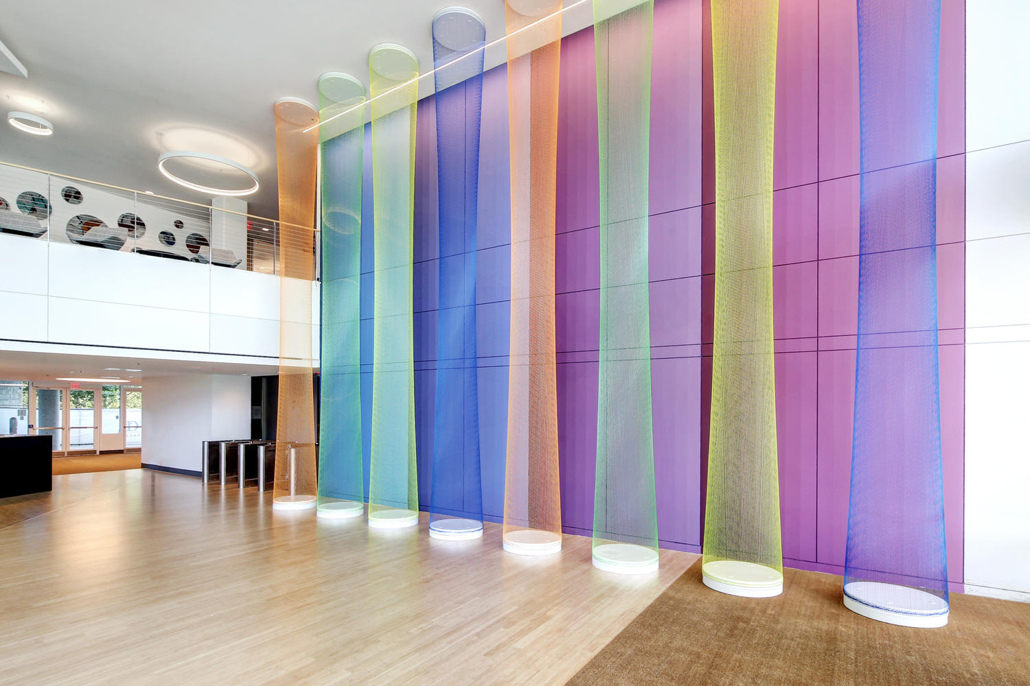 Colorful vertical fabric panels in a modern interior space with wooden flooring and white walls.
