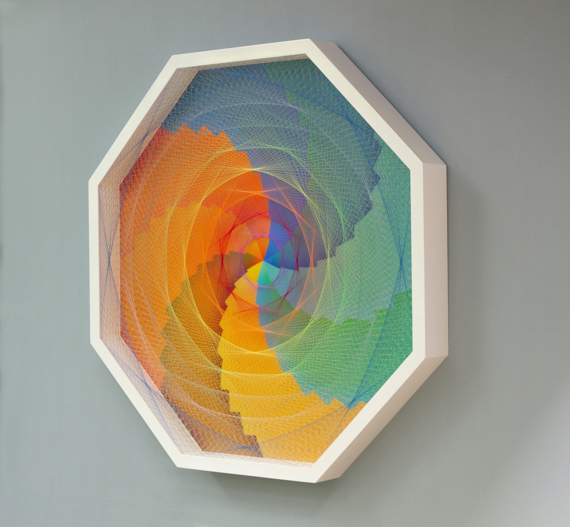 Colorful geometric spiral artwork in an octagonal frame on a wall.